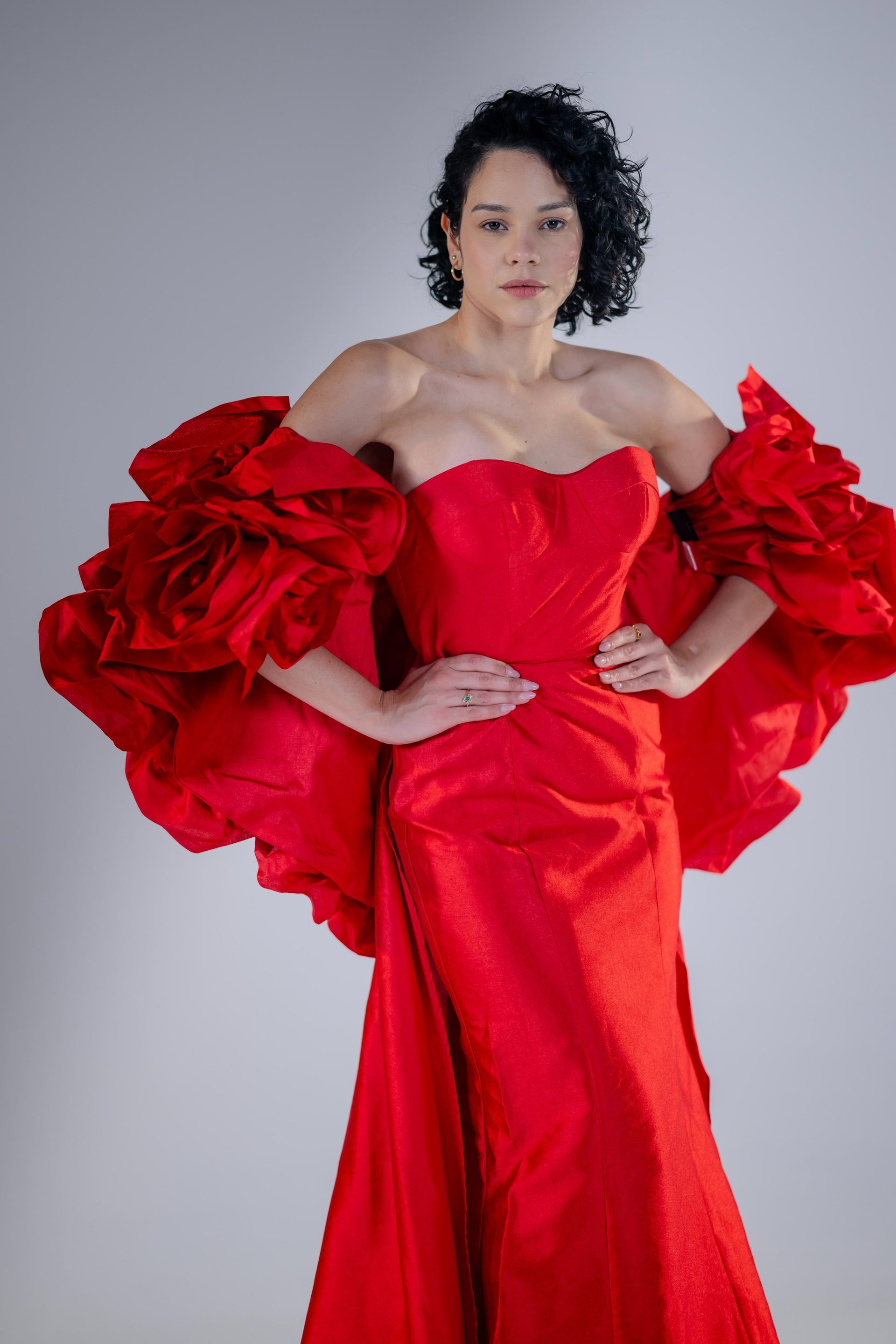 Woman in a bright red ruffled gown posing against a plain gray background