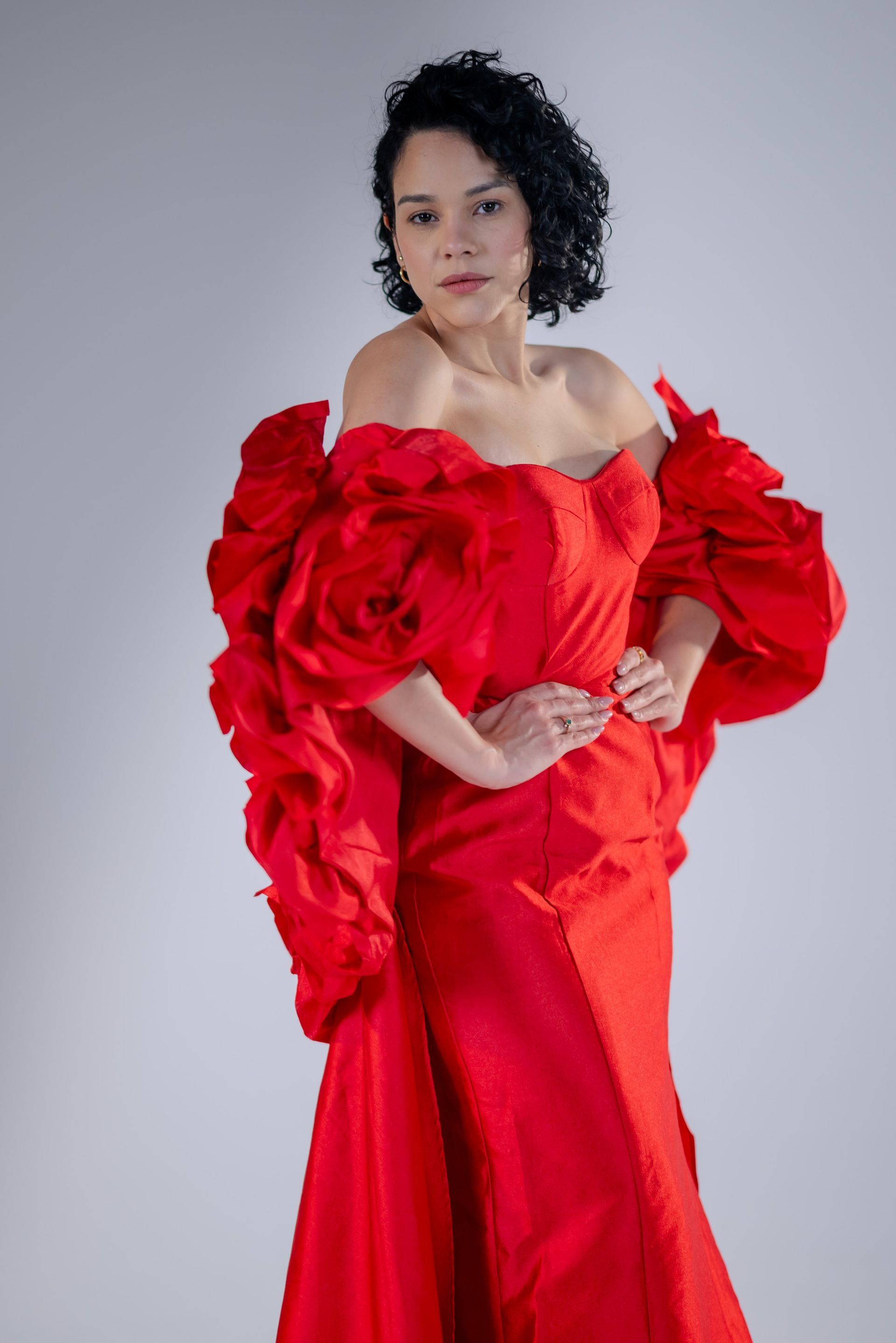 Person in a bright red ruffled gown, posing against a plain gray background.