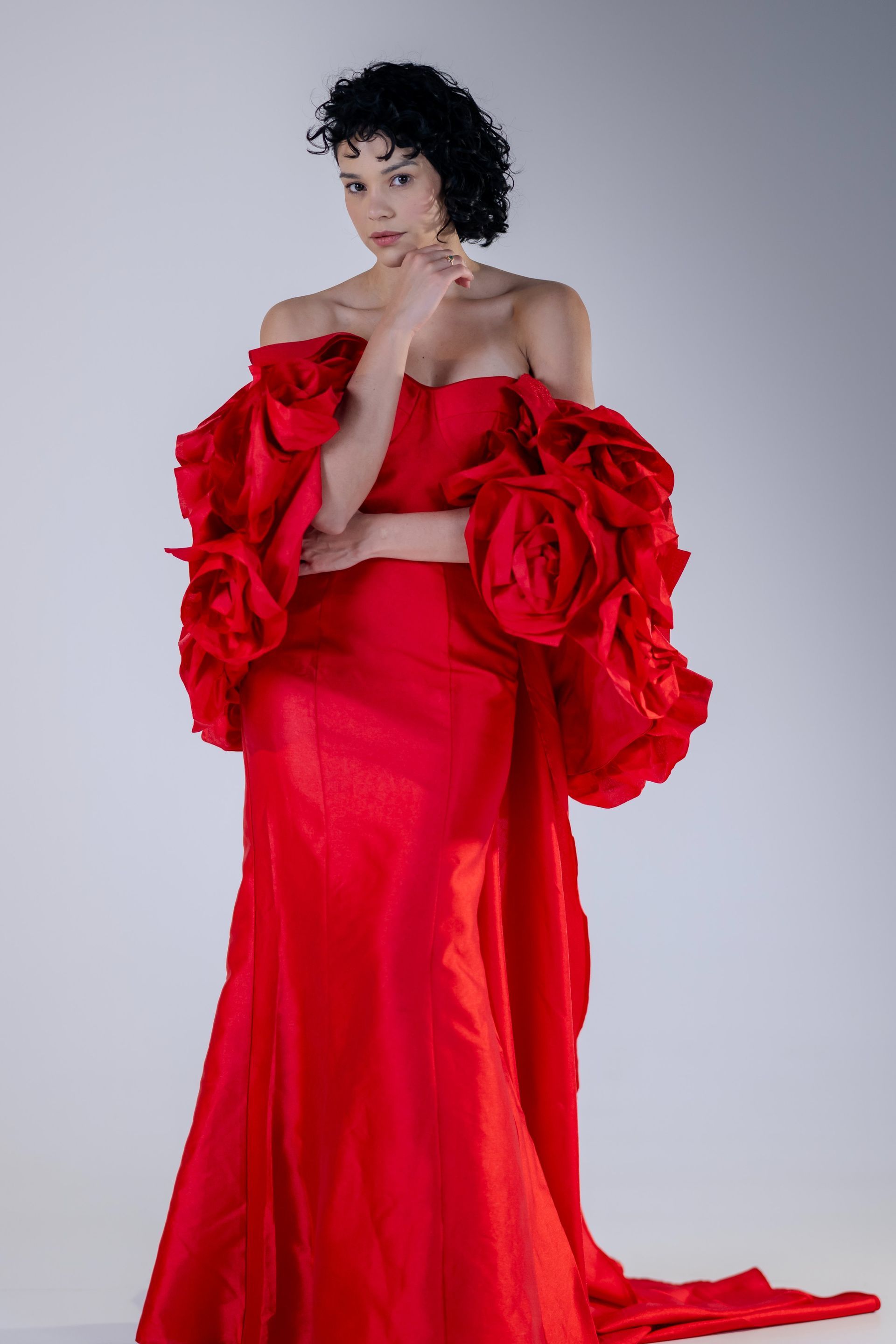 Model in a bright red ruffled gown posing against a gray studio backdrop