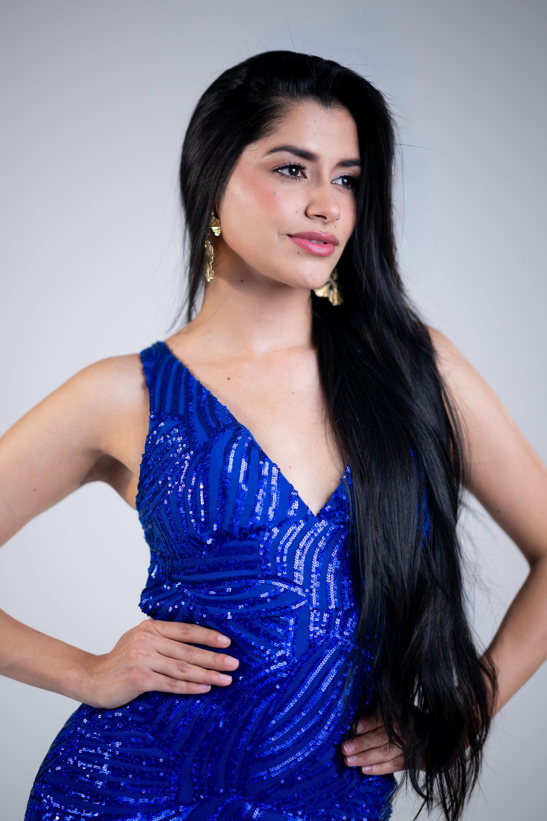 Woman in a blue sequined dress posing with hand on hip against a gray background