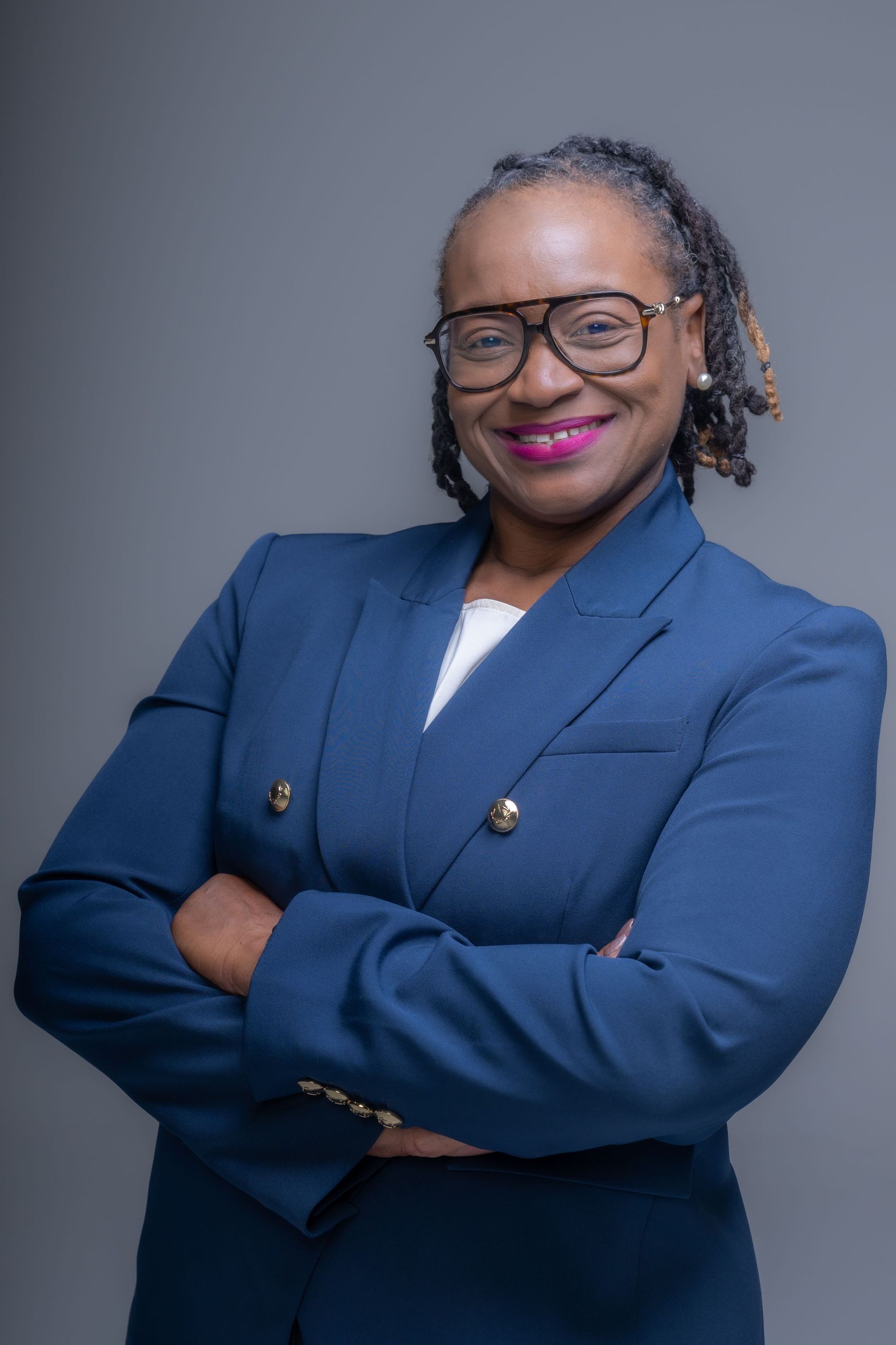 Smiling professional in a navy blazer with arms crossed against a gray background