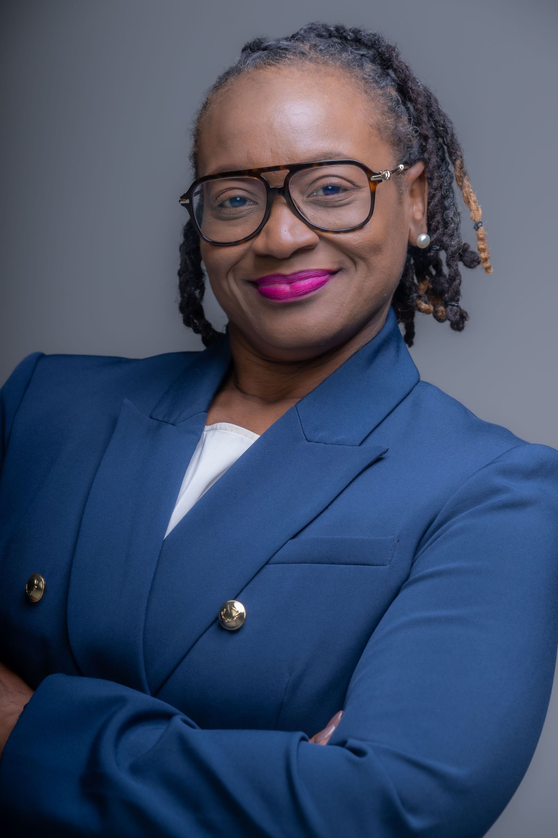 Portrait of a smiling person in a blue suit and glasses with folded arms against a gray background