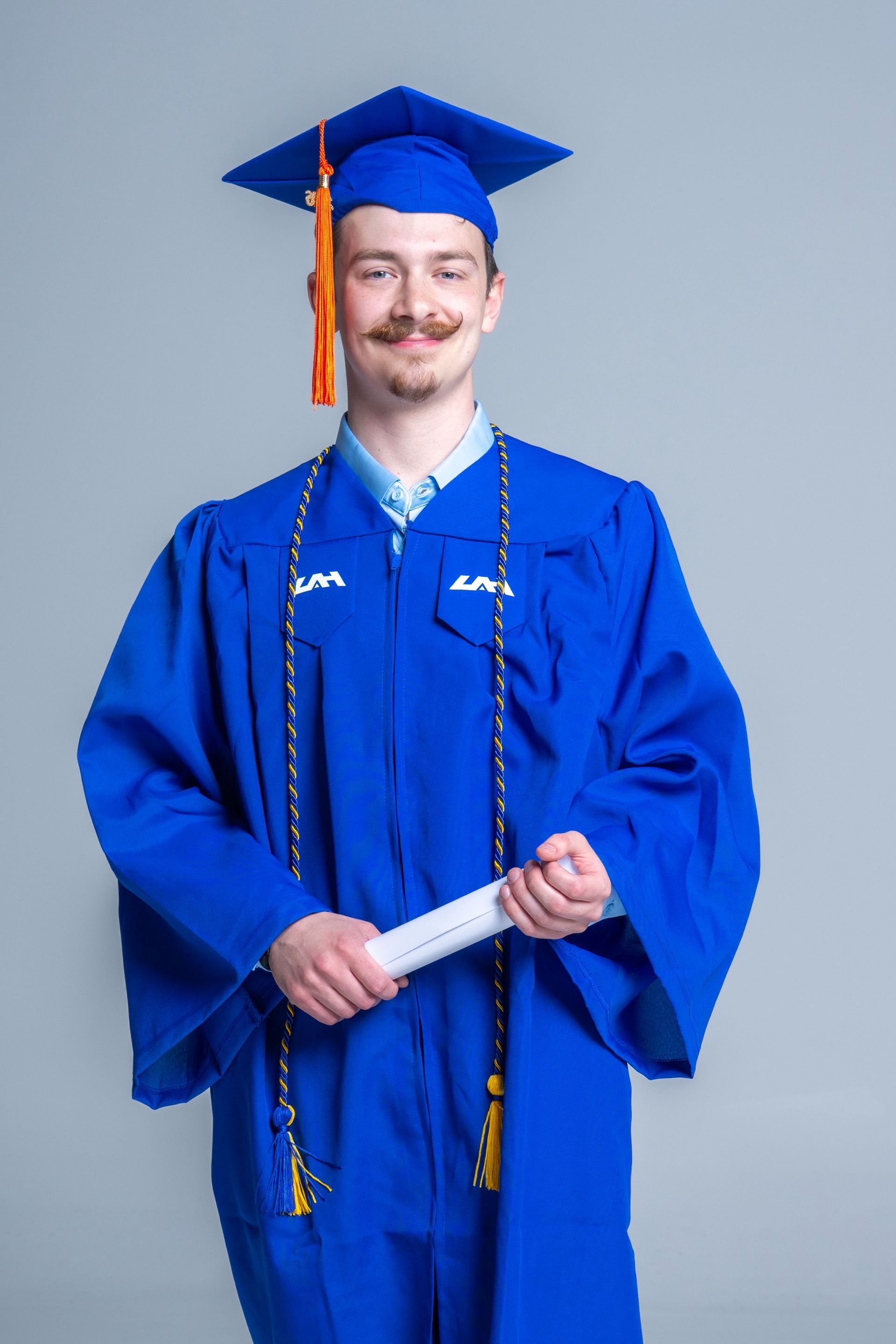 Person in blue graduation cap and gown holding a diploma against a gray background