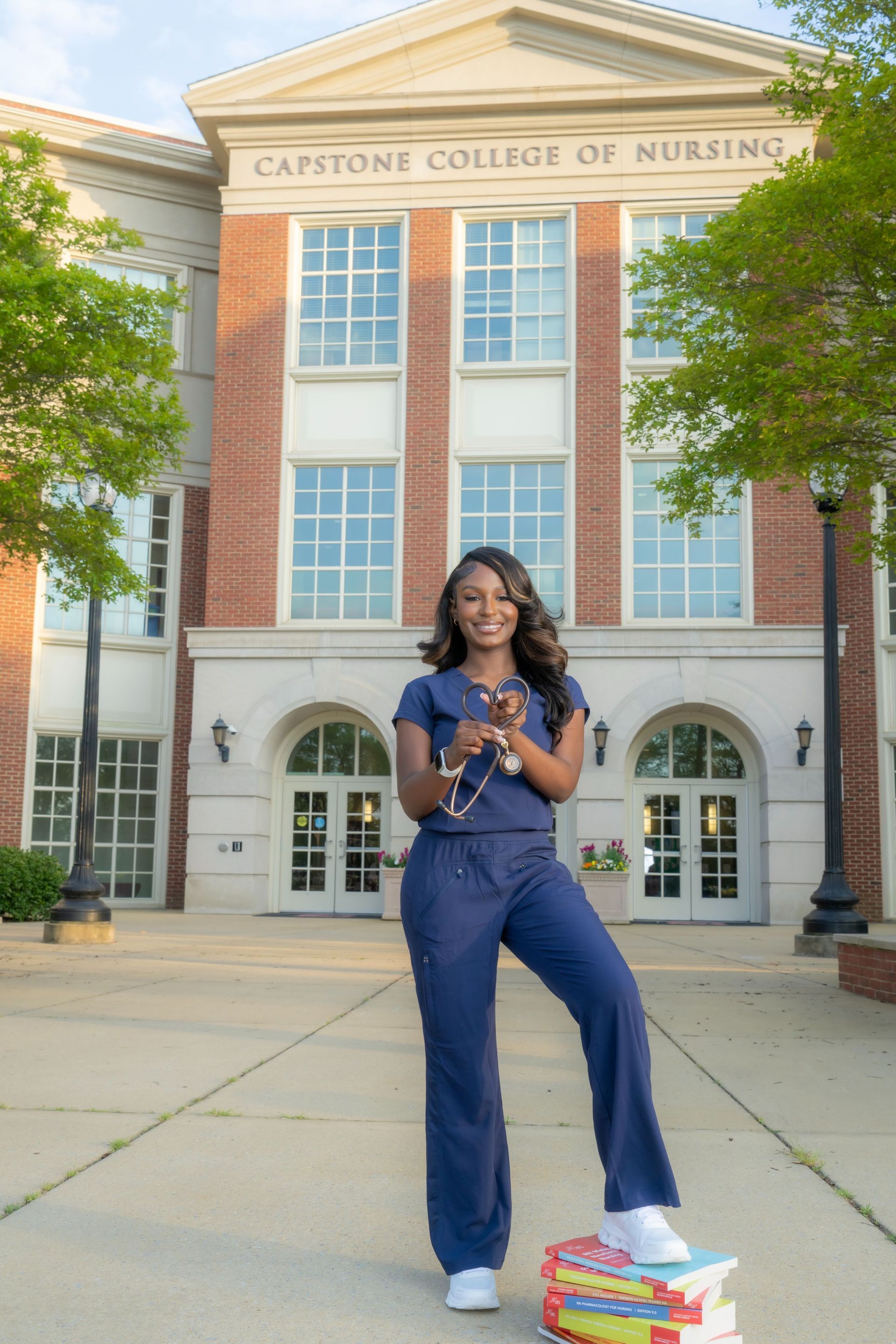 Woman standing in front of a nursing college building, holding flowers in a blue outfit.