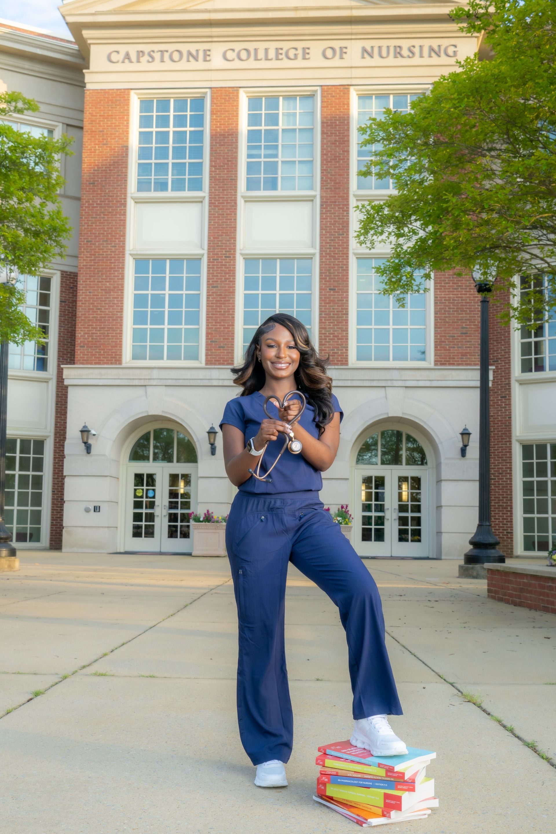 Woman standing outside a nursing college building, holding a diploma with books at her feet.