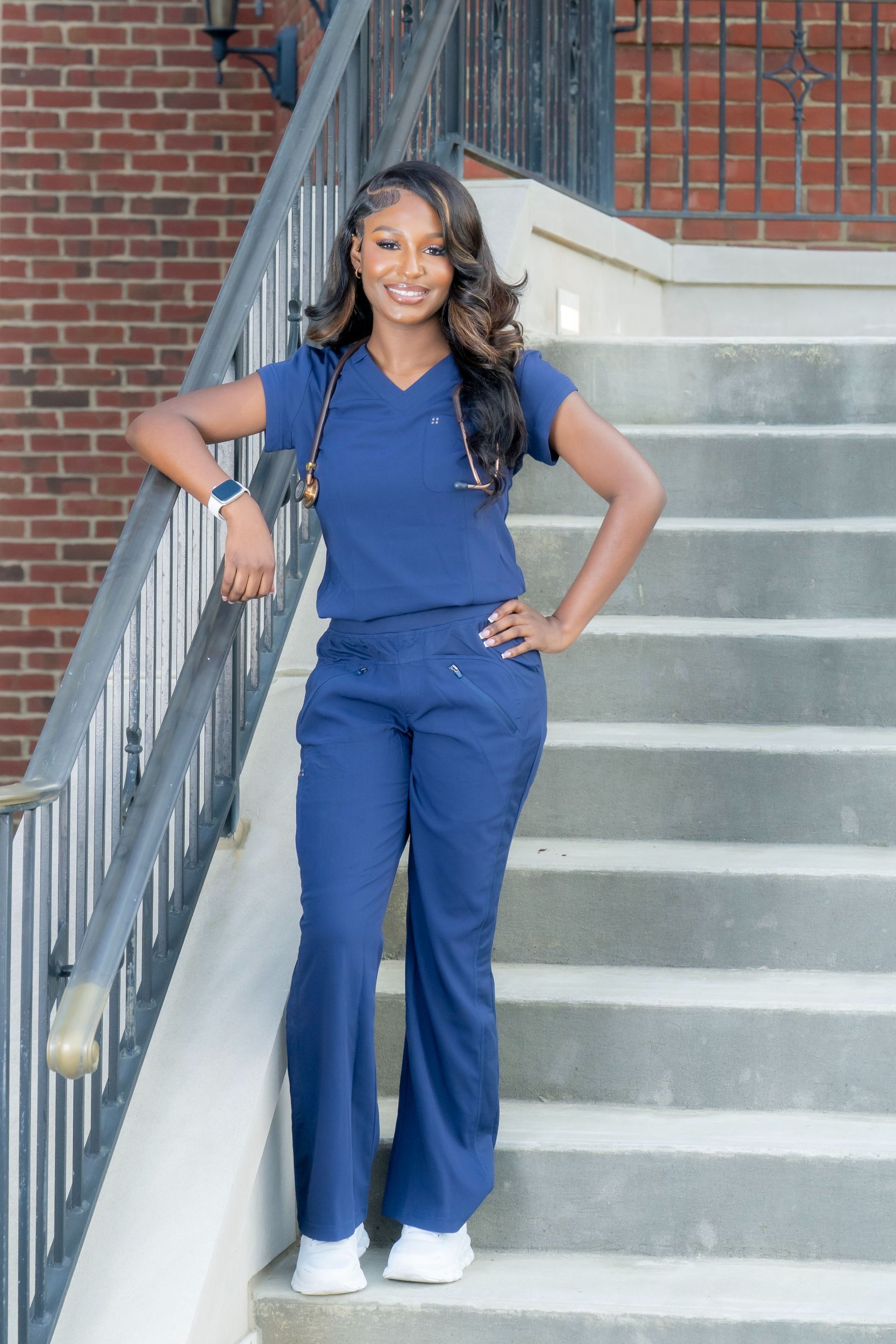 Woman in navy outfit standing on outdoor steps, leaning on the railing and smiling.