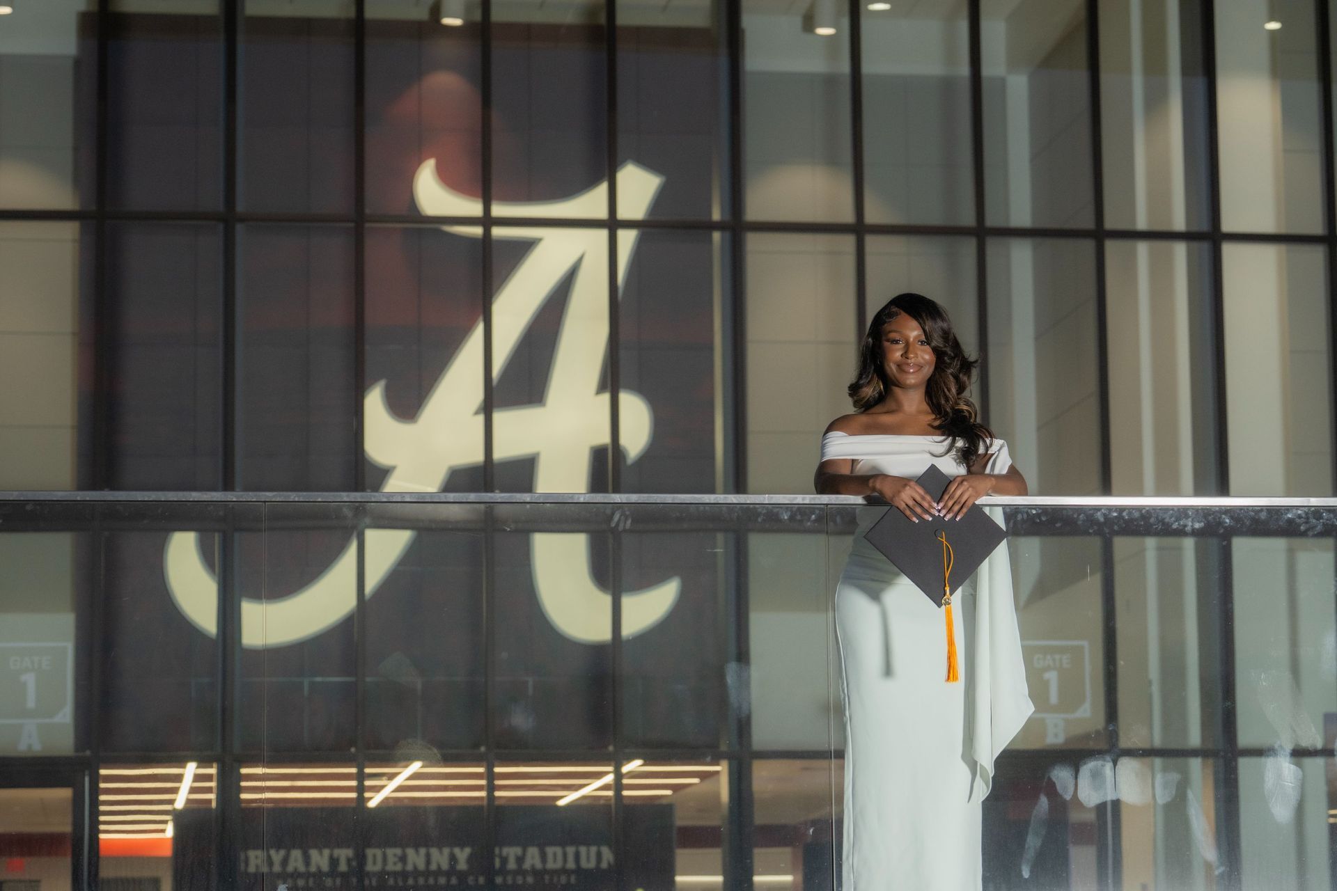 Woman in a white gown standing before a large illuminated Alabama A logo on a glass wall.