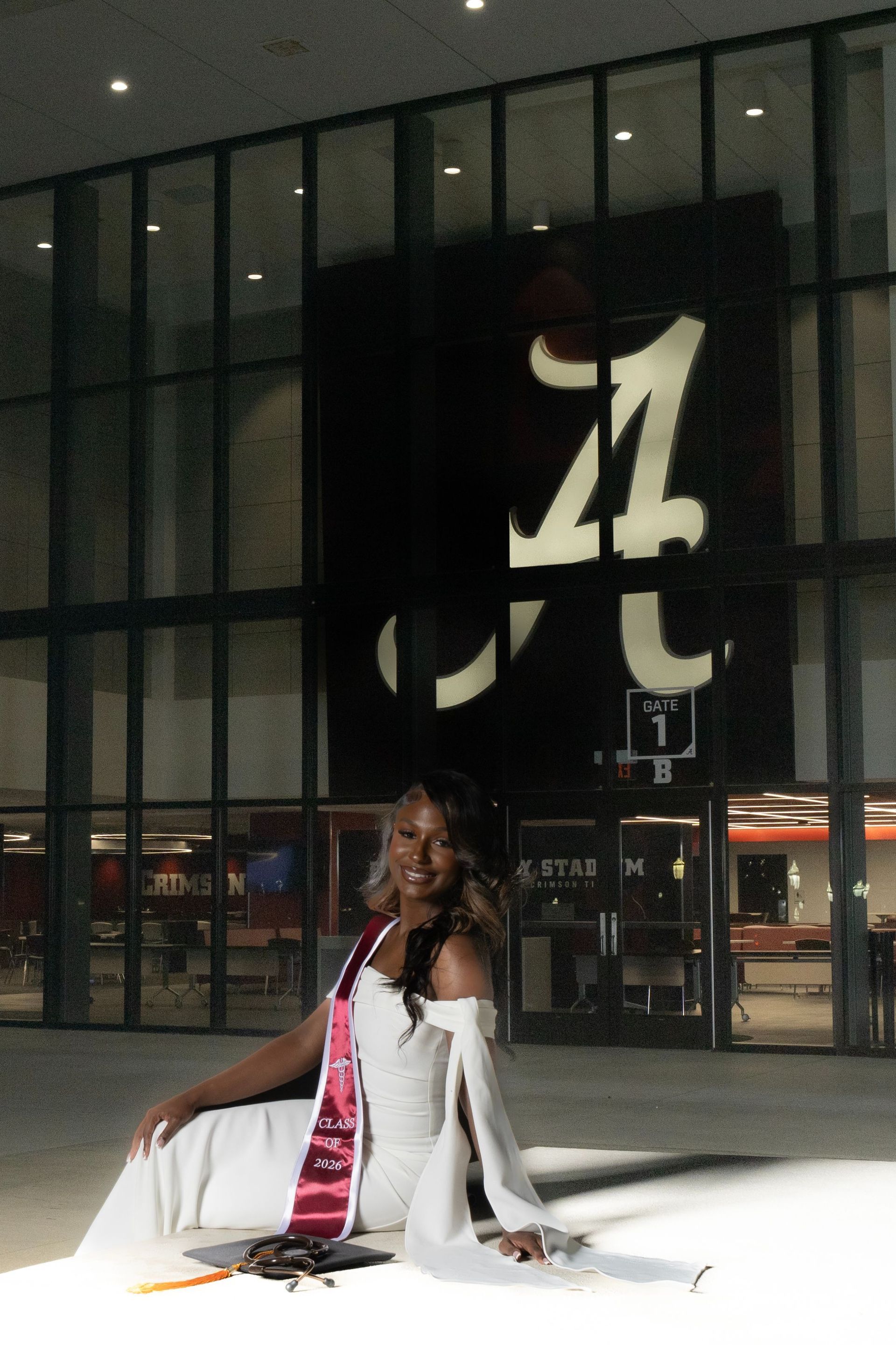 Woman in a white outfit posing on a runway in front of a large stadium entrance sign at night
