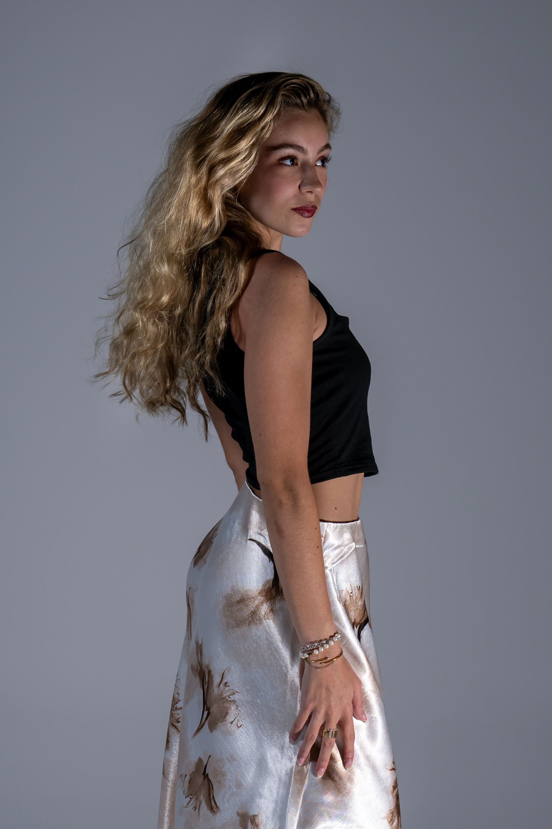 Woman in a black top and silver skirt posing in profile against a gray background