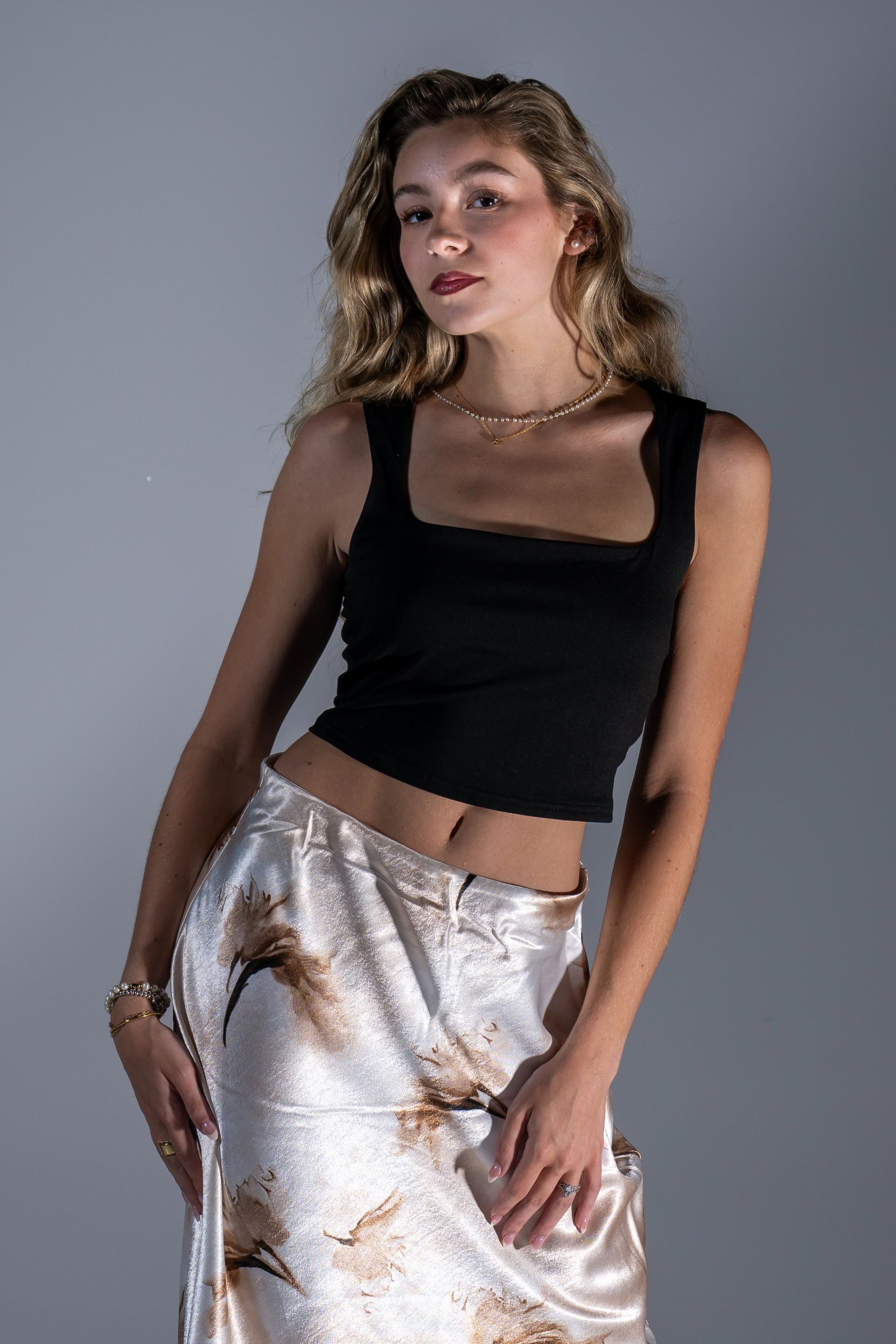 Woman posing in a black tank top and satin skirt against a gray studio backdrop