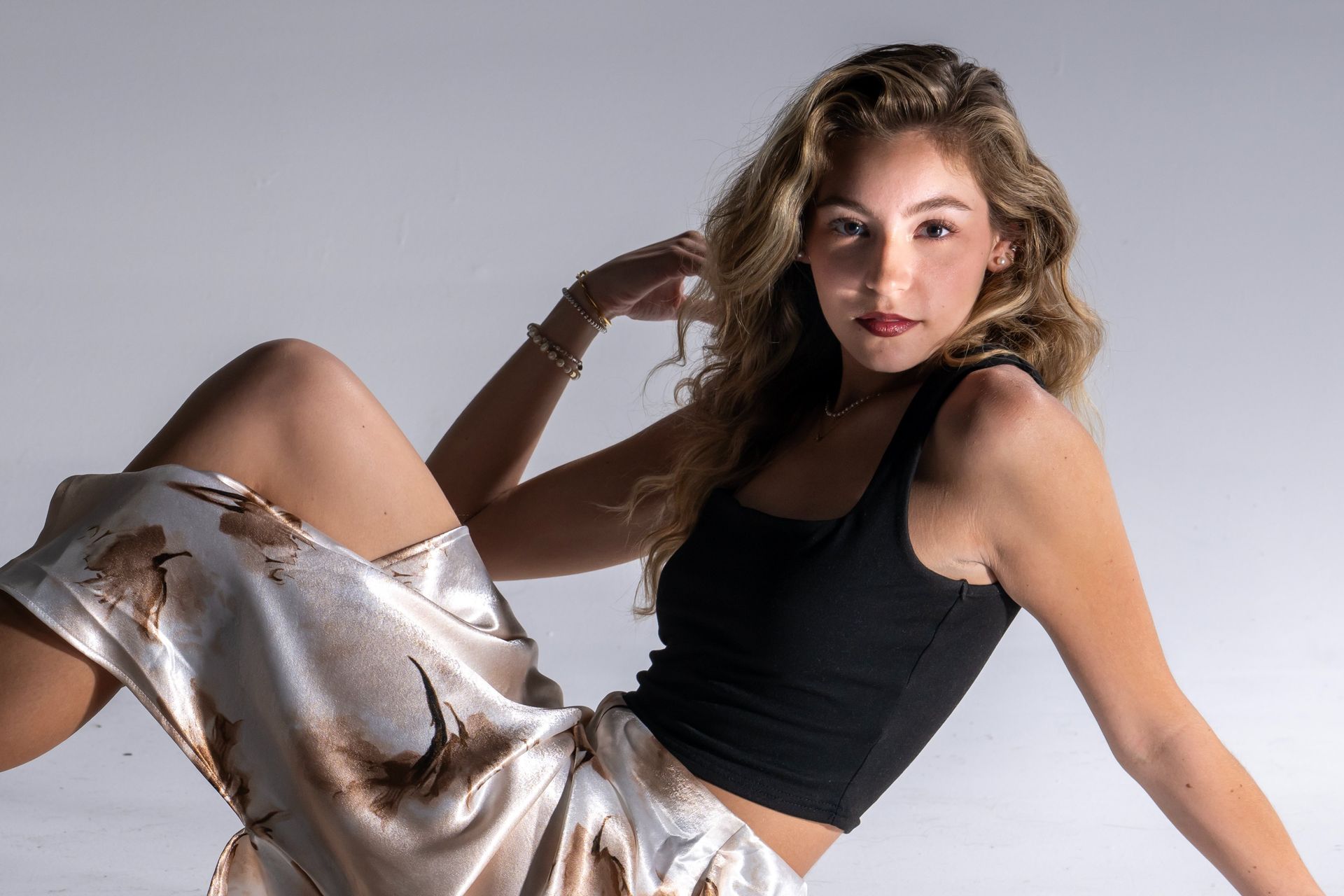 Woman posing on a gray studio backdrop in a black top and silver skirt