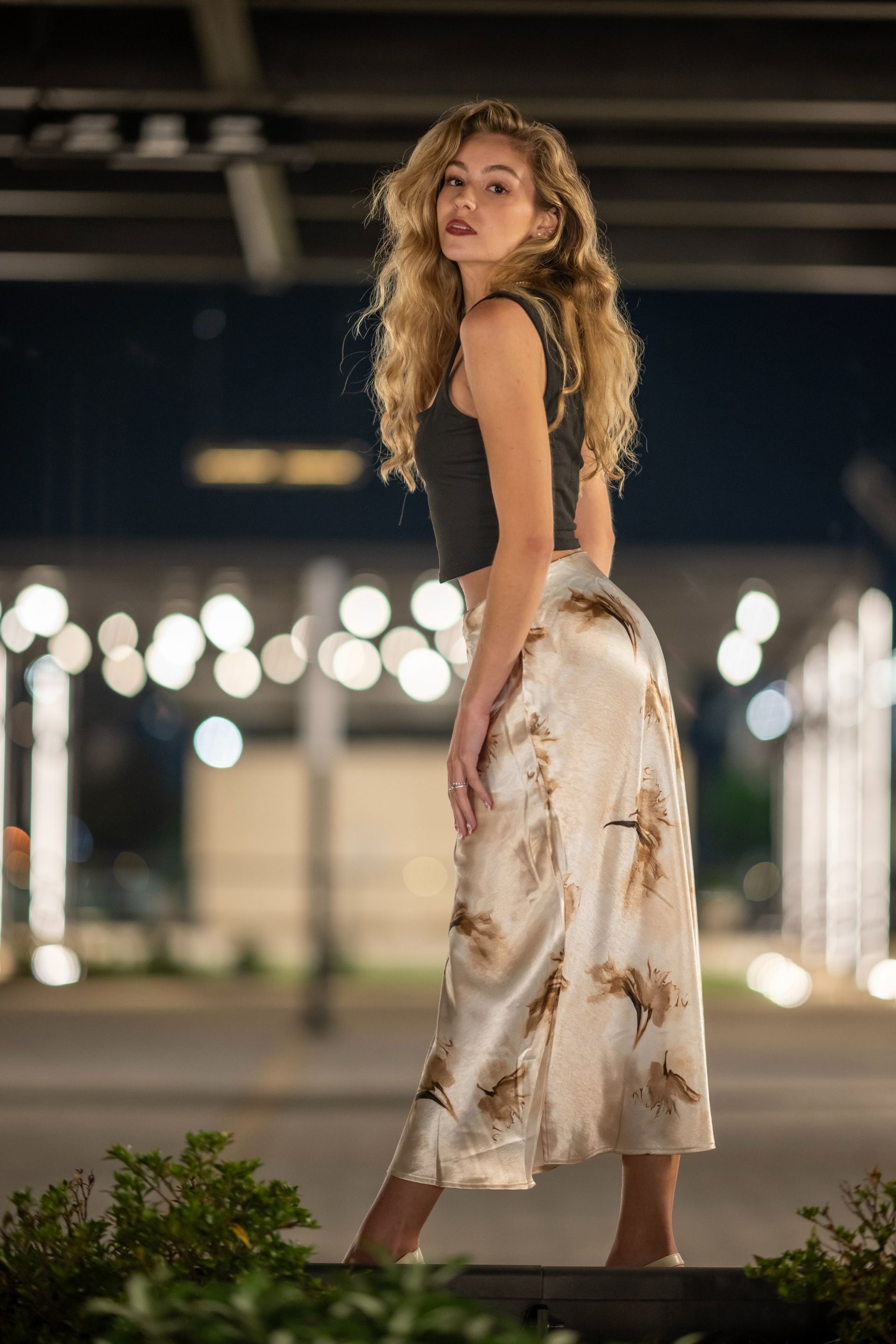 Woman in a white floral dress posing outdoors at night with blurred lights in the background