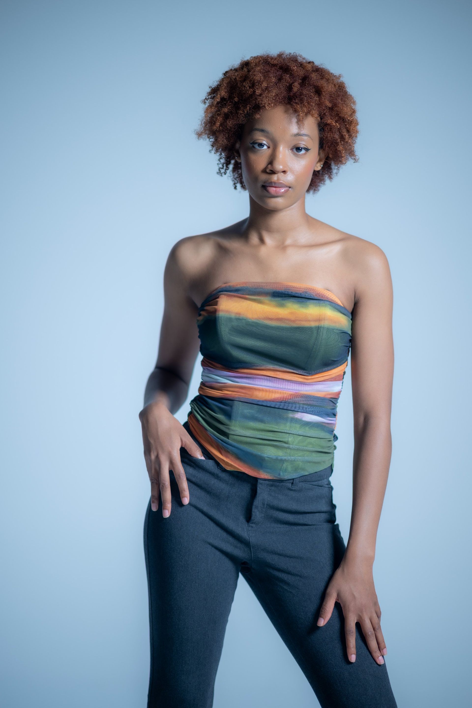 Studio portrait of a person in a colorful strapless top and jeans against a blue background