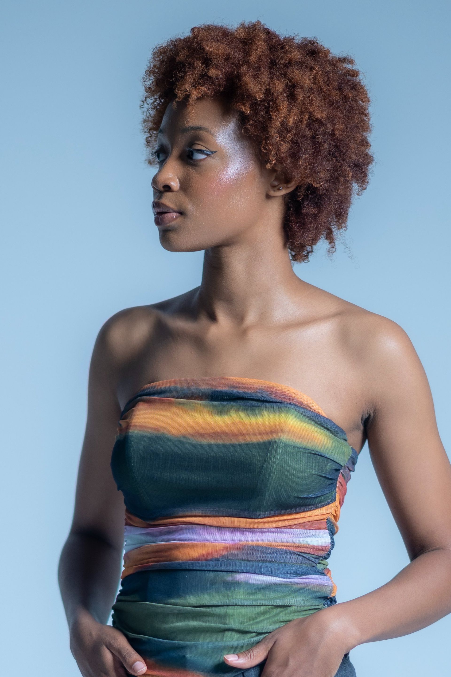 Woman in a colorful strapless dress against a light blue background, facing left.
