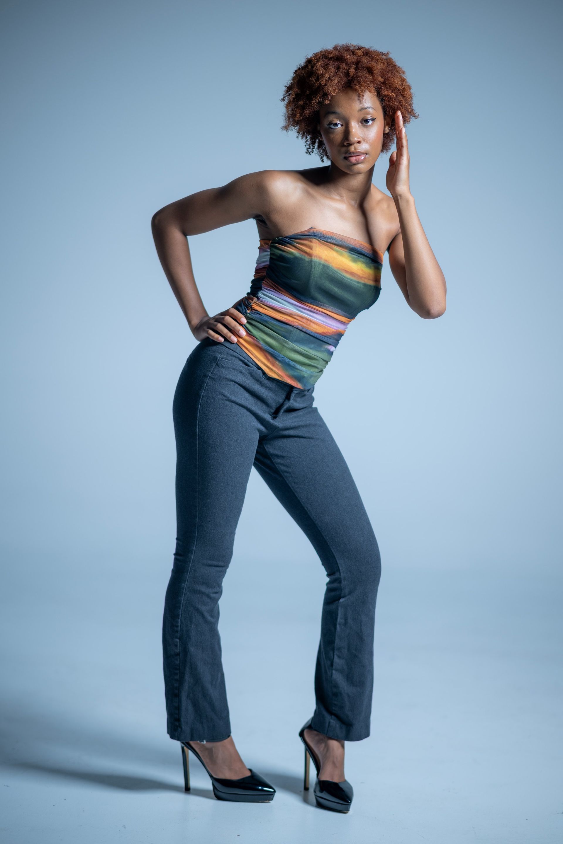 Woman posing in a striped top, jeans, and black heels against a light blue studio backdrop