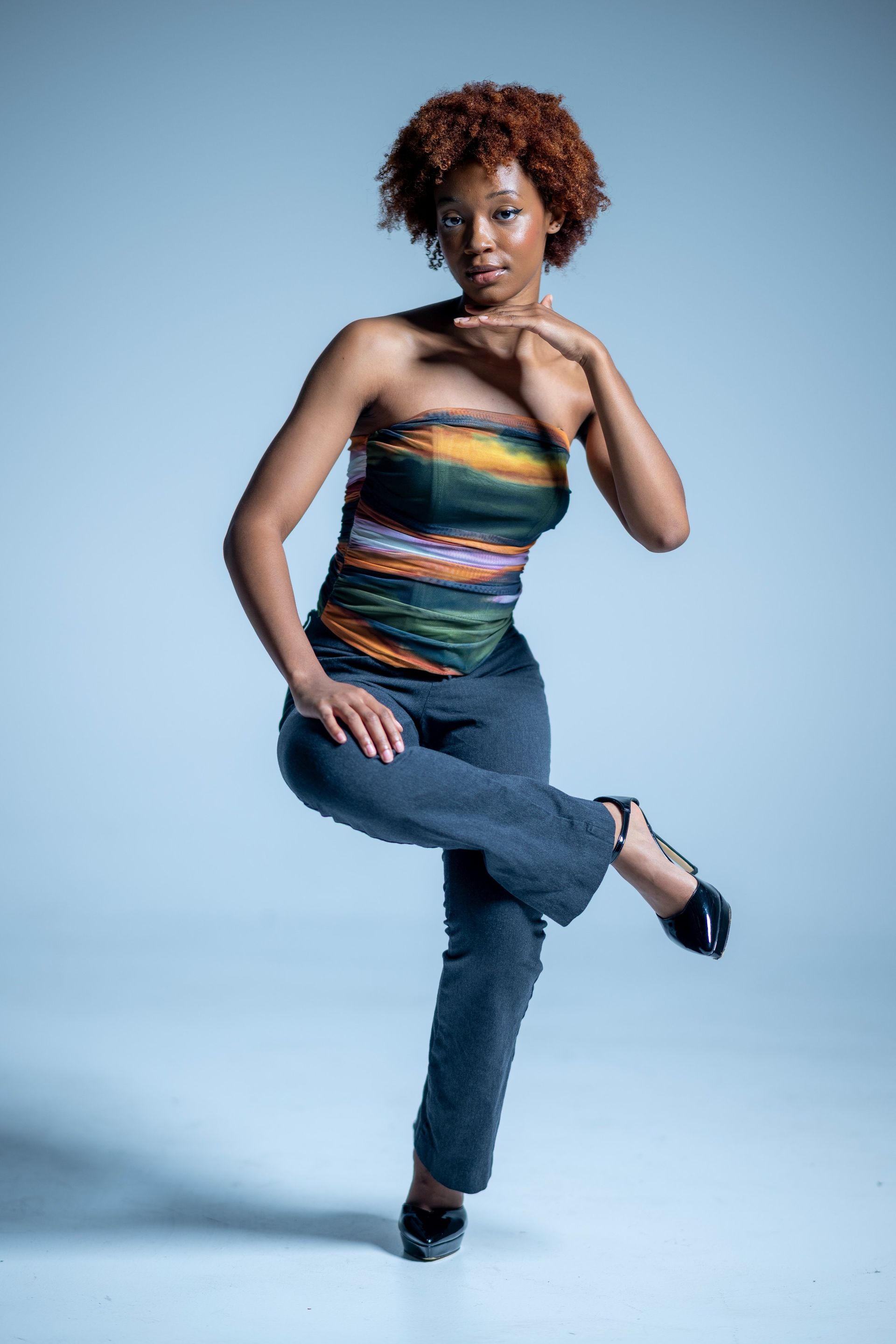 Person posing in a colorful striped top and jeans against a light blue studio background