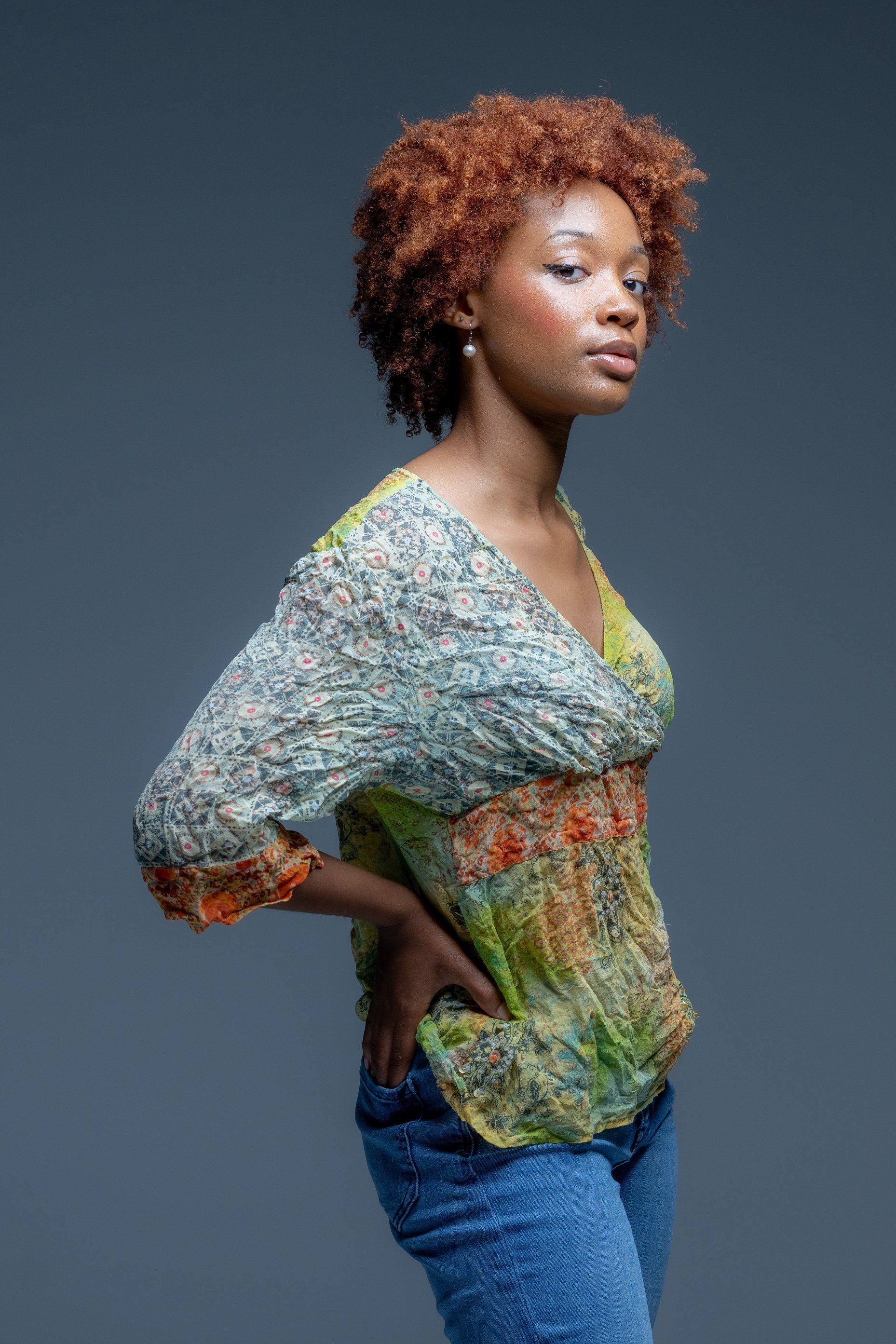 Portrait of a person posing in a patterned shawl and blue jeans against a dark gray background