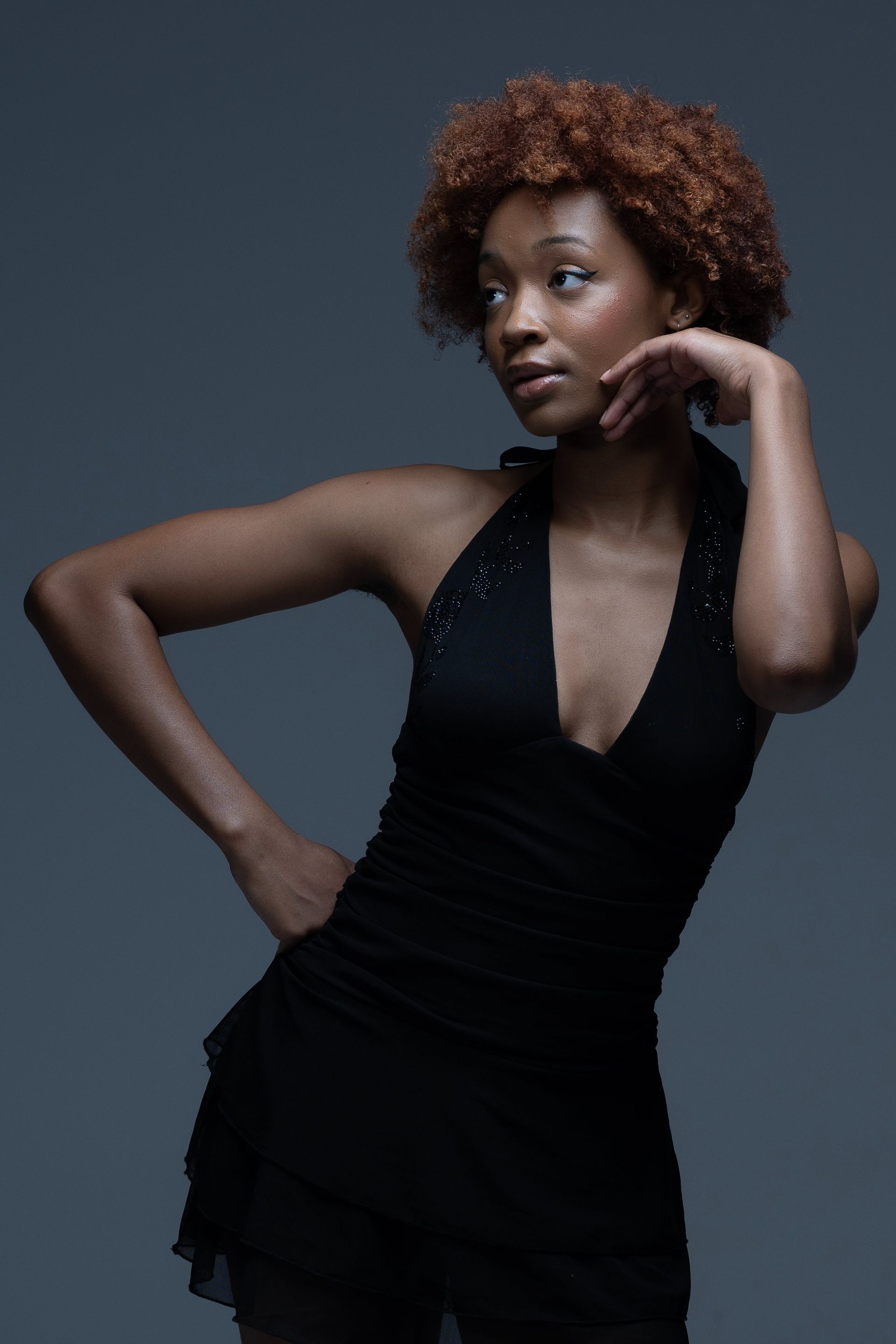 Woman in a black dress posing against a dark gray studio backdrop.