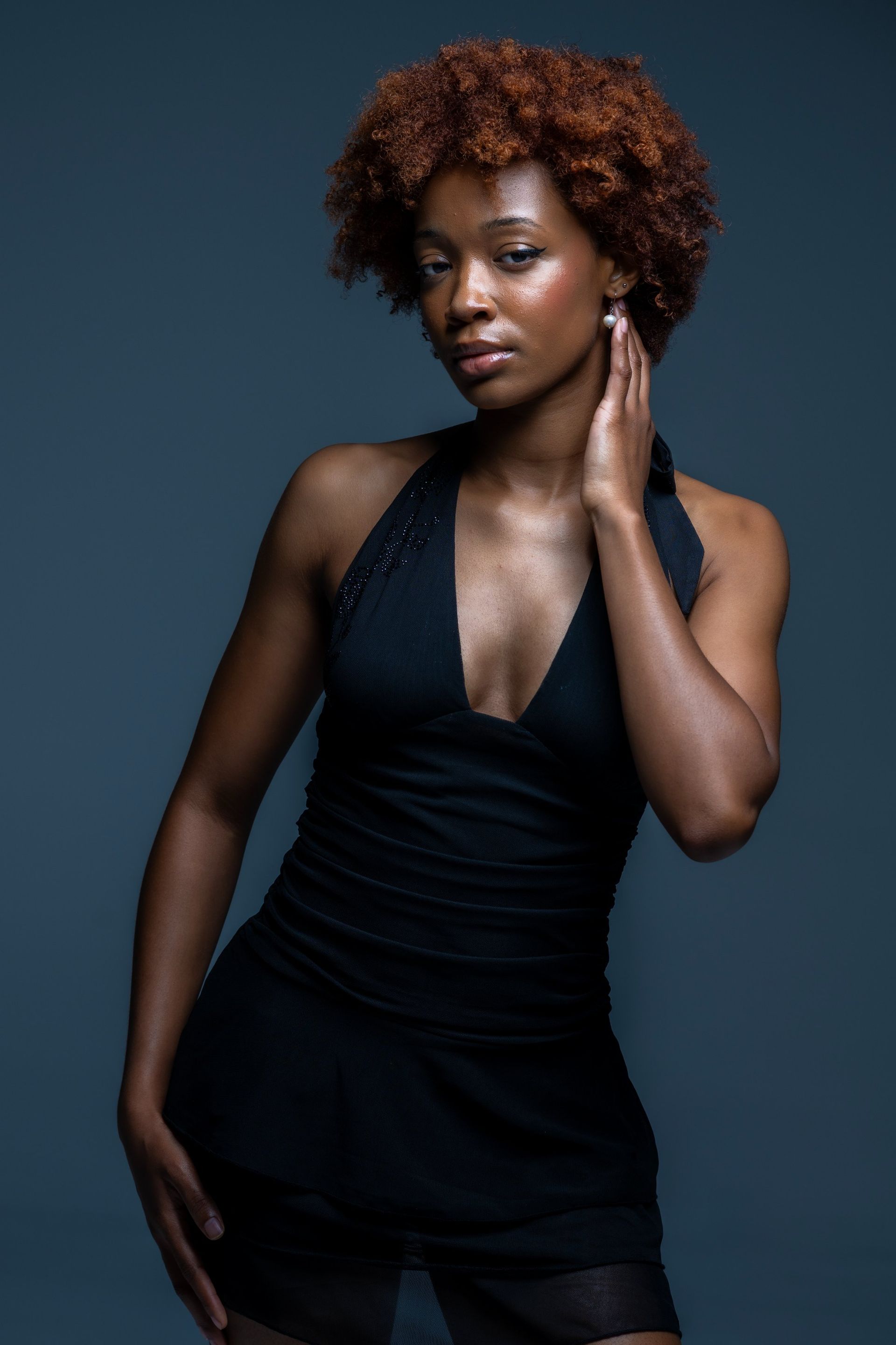 Woman in a black dress posing against a dark studio backdrop.