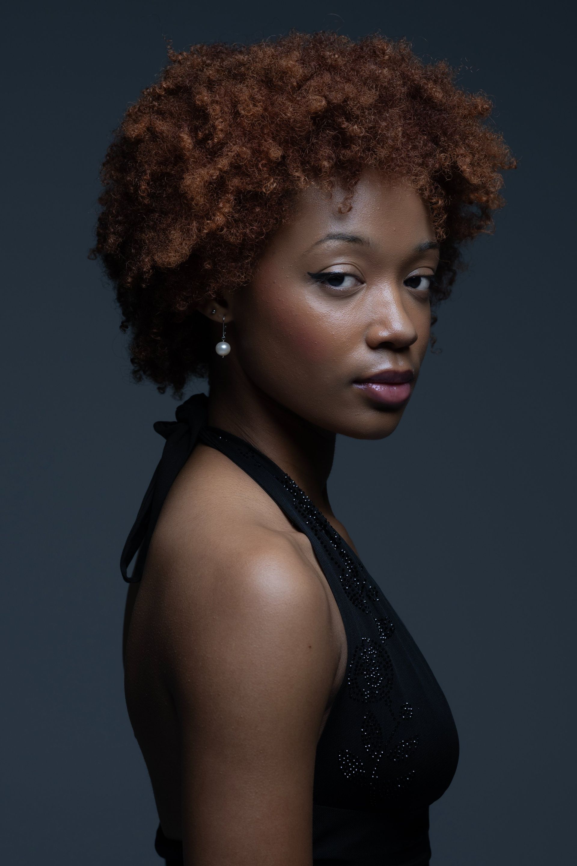Portrait of a woman in a black dress against a dark background, looking over her shoulder.