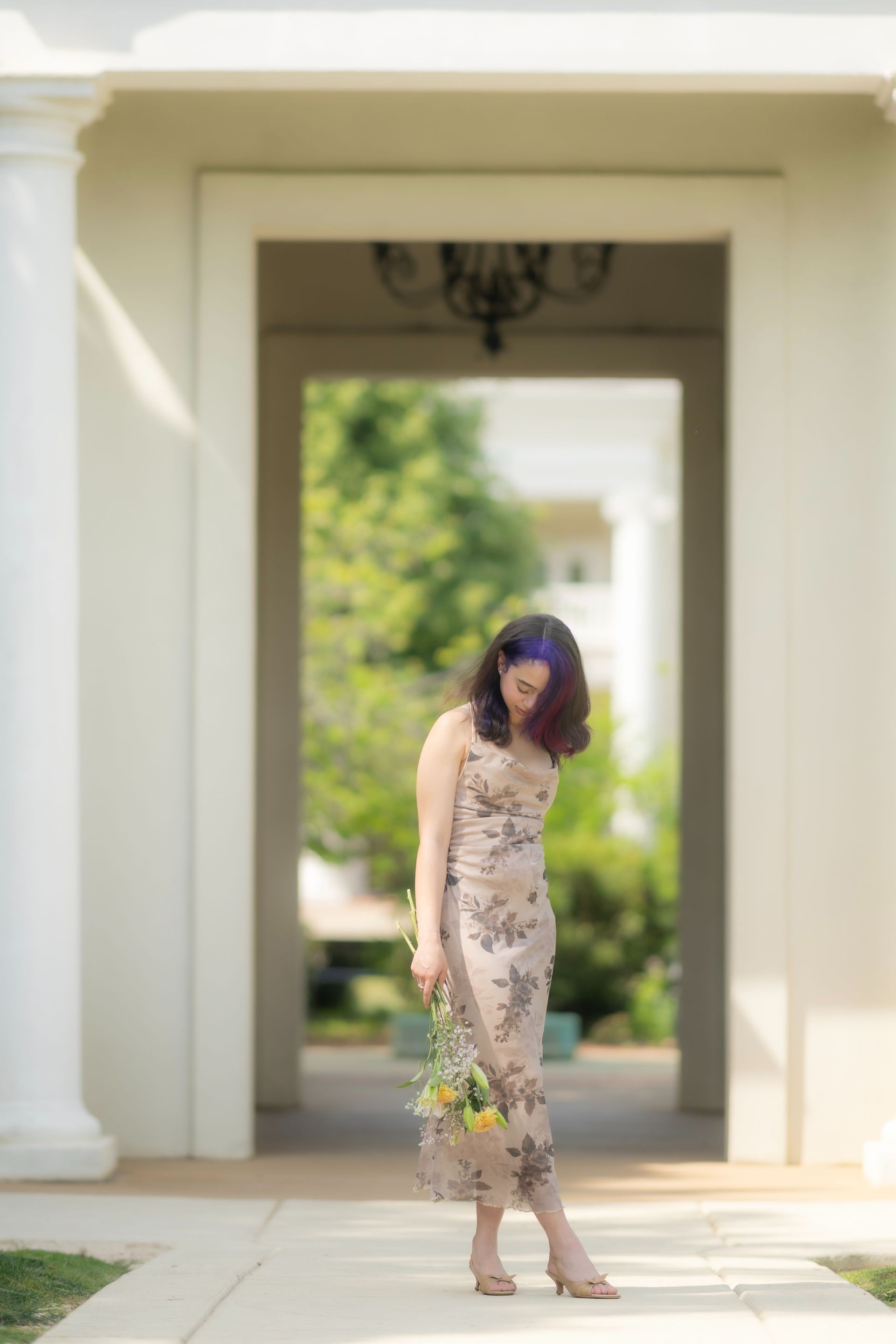 Woman in a floral dress standing in a sunlit courtyard framed by white columns