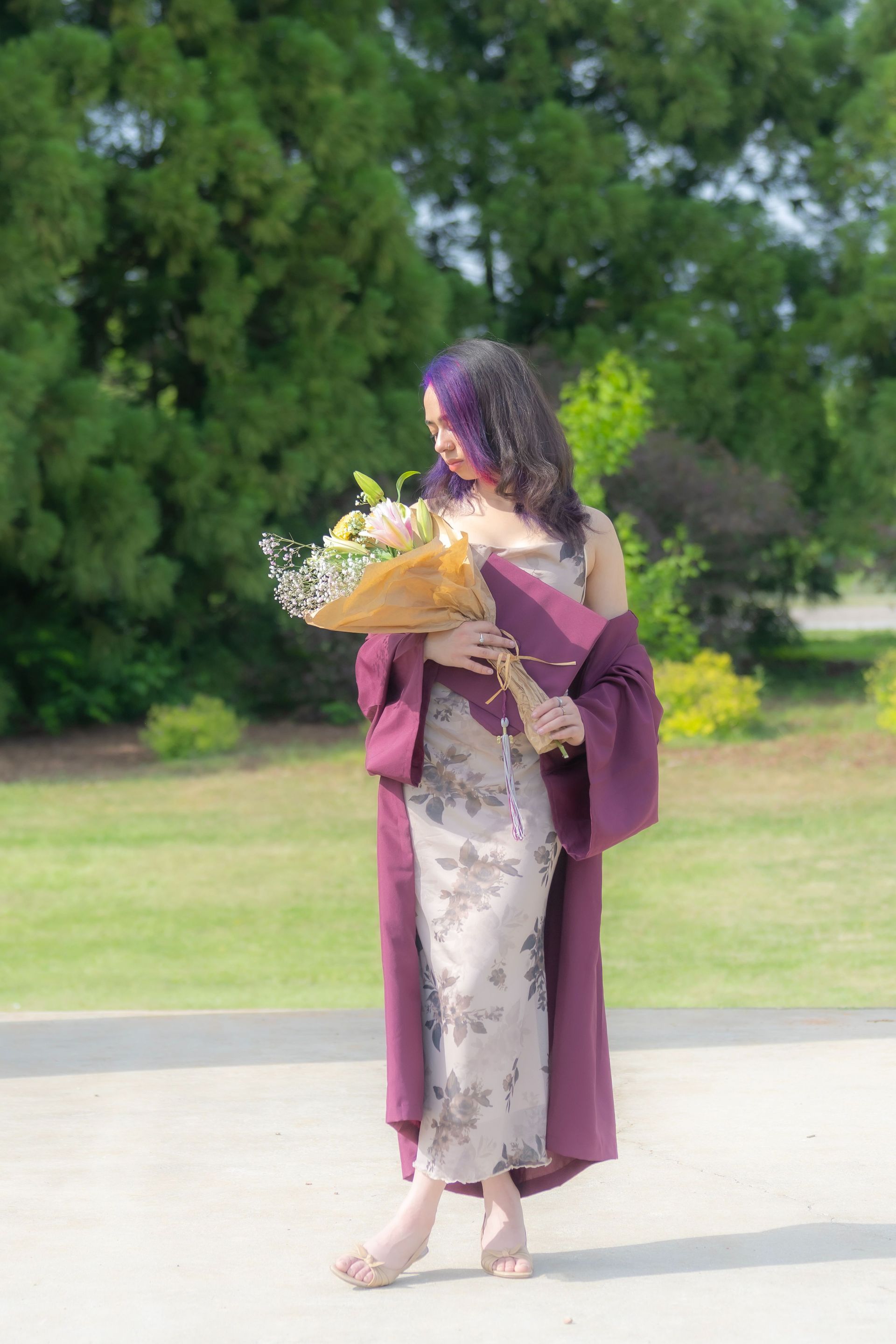 Woman in a lavender dress and maroon shawl holding a bouquet outdoors on a sunny day
