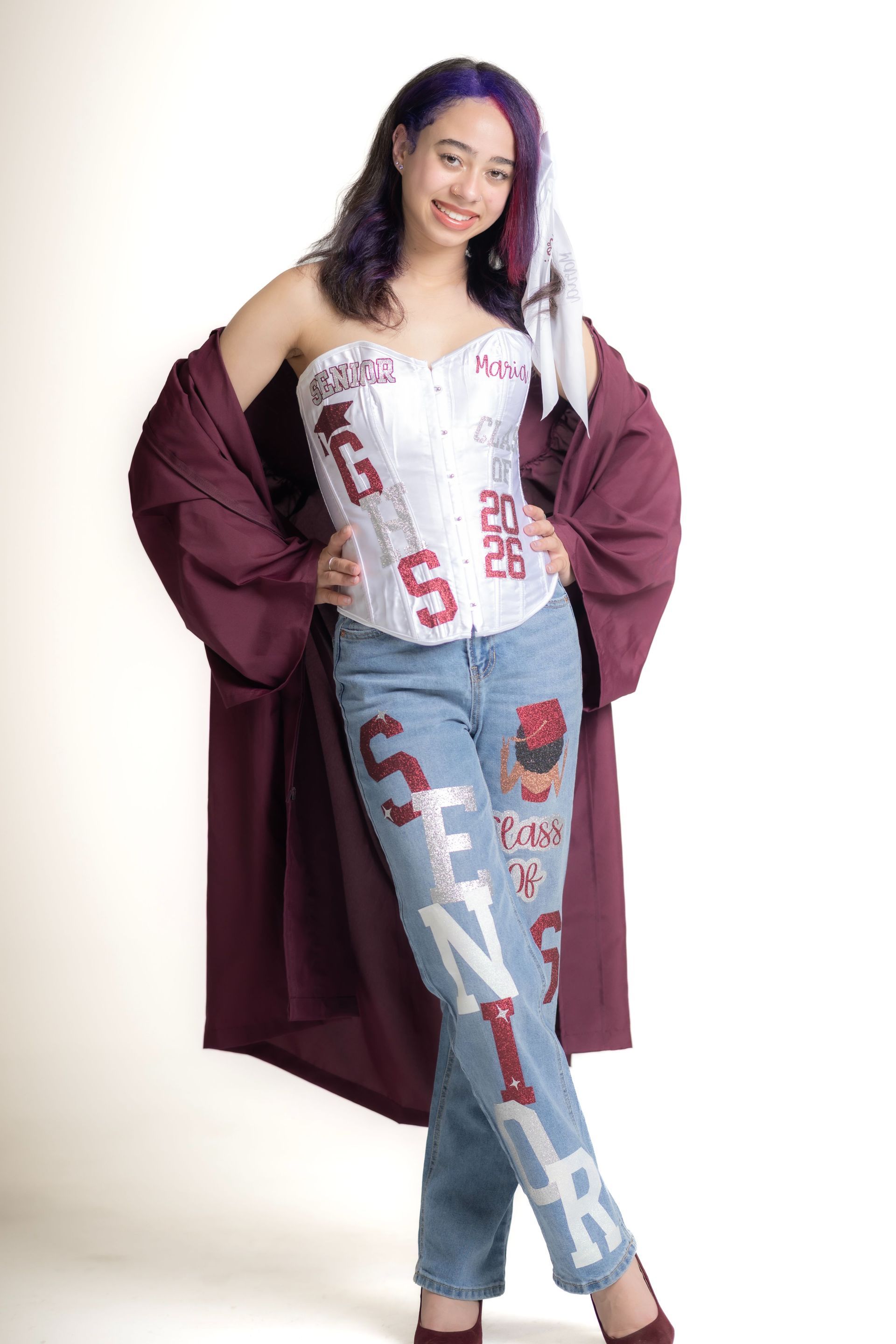 Fashion model posing in a burgundy coat, white top, and light blue jeans against a white background
