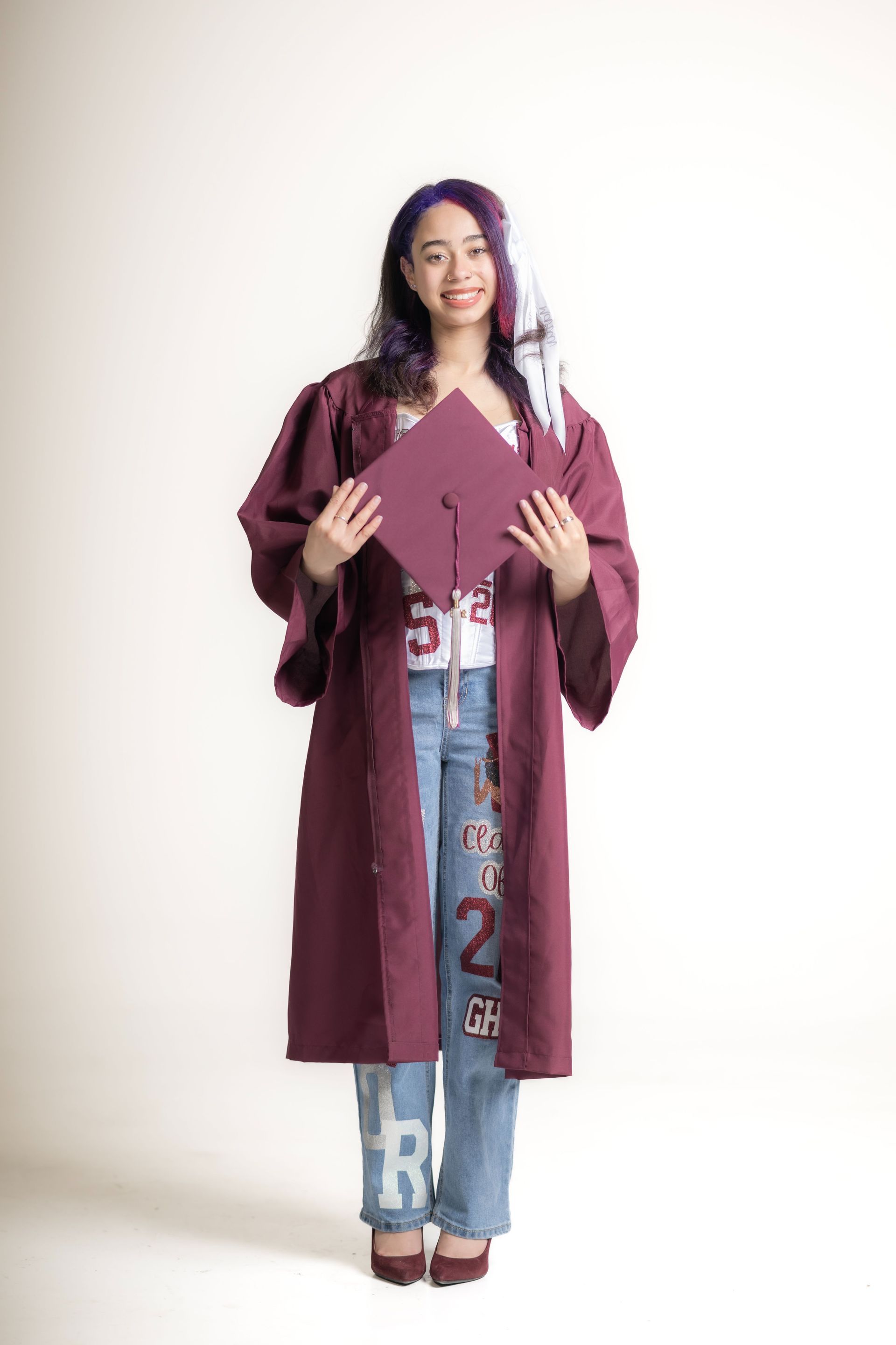 Woman in a burgundy robe holding a maroon folder, standing against a plain white background.