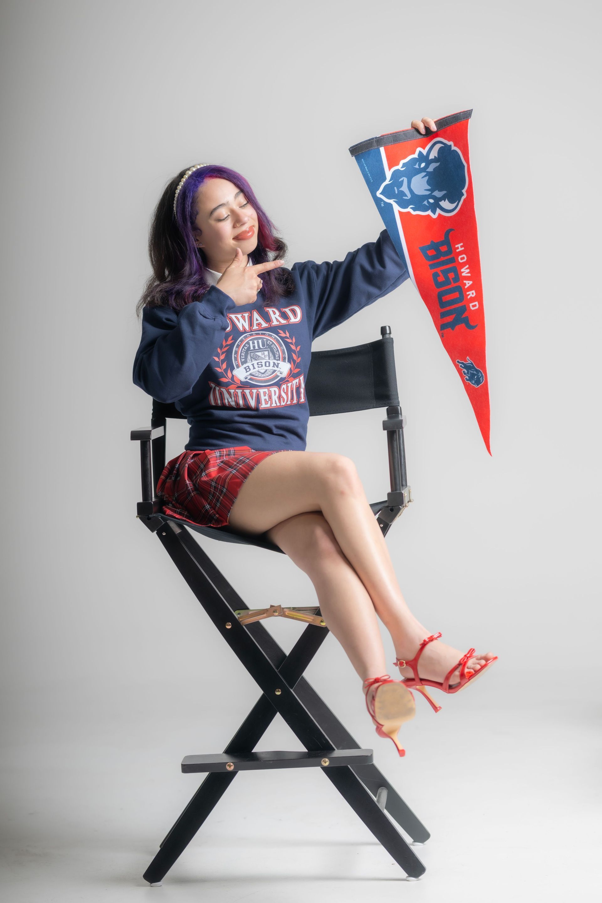 Woman seated on a director’s chair holding a red and blue pennant, in a studio setting.