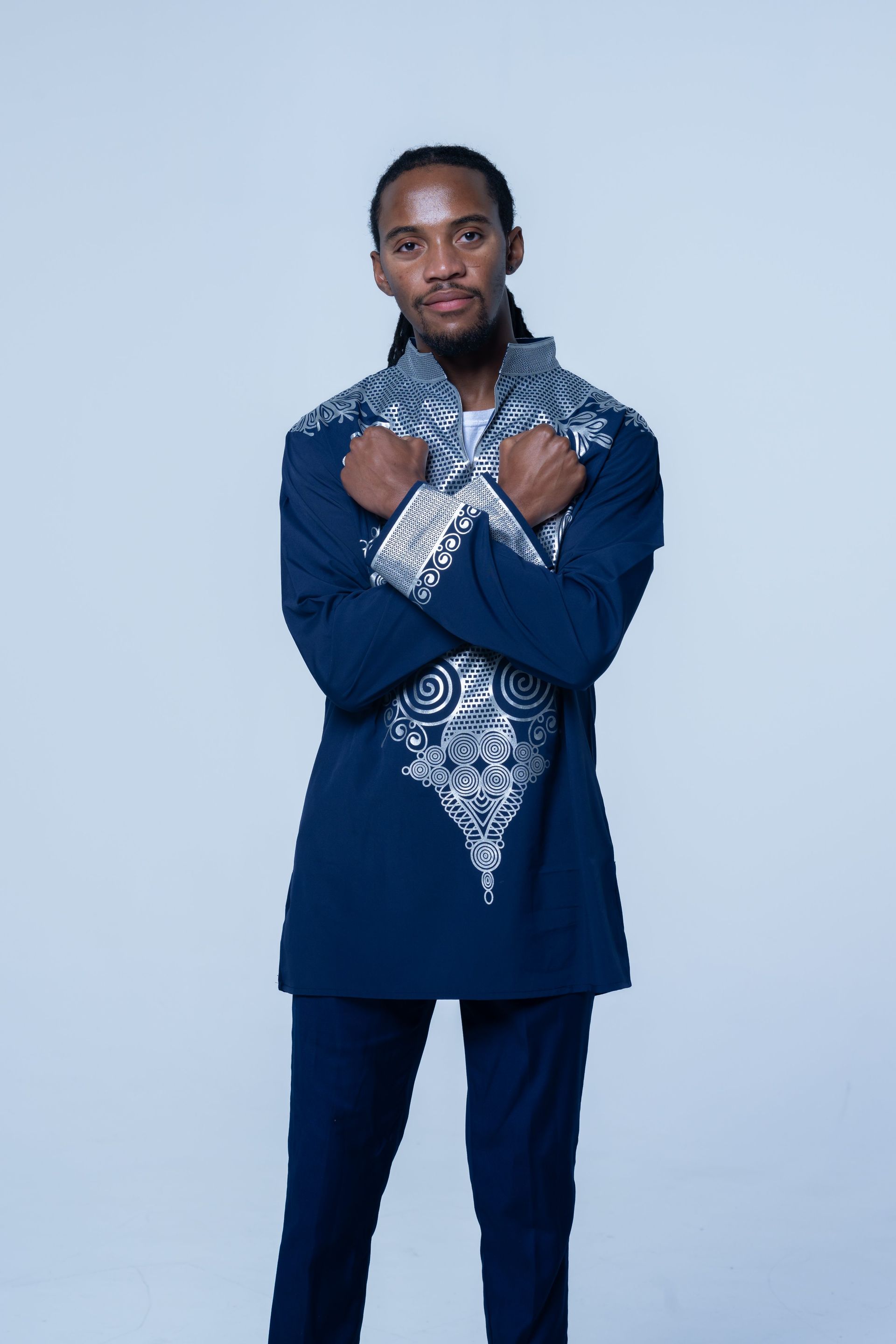 Person standing against a light blue backdrop, wearing a navy outfit and patterned scarf, hands raised near chest.