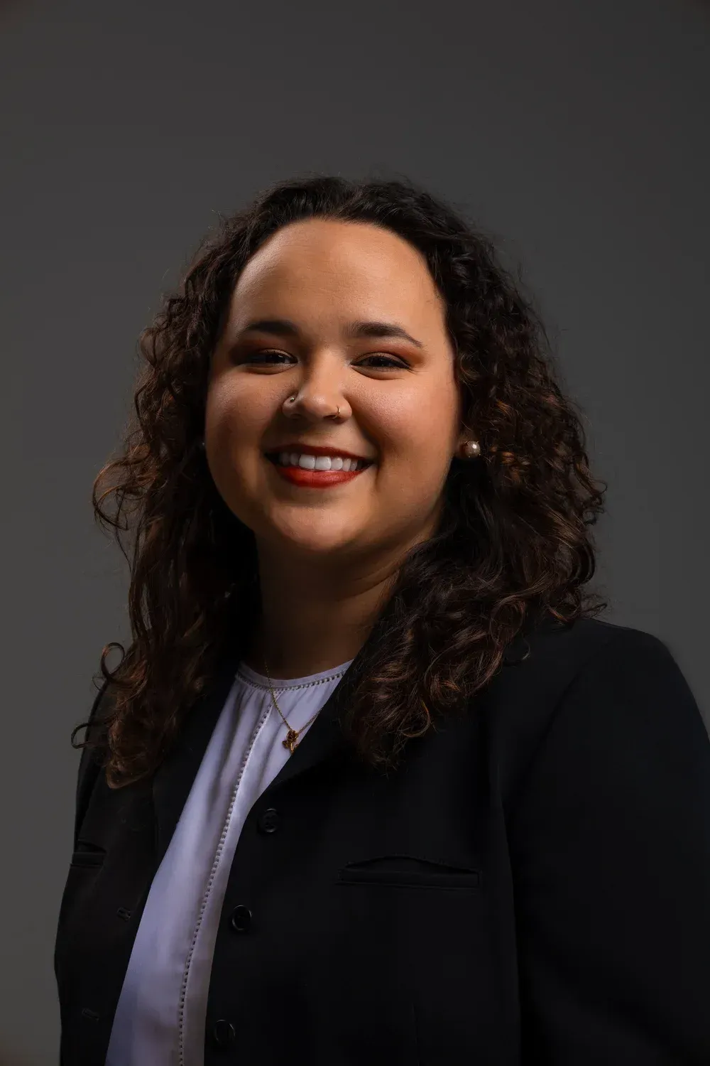 Smiling person in a black blazer and white top against a dark gray background