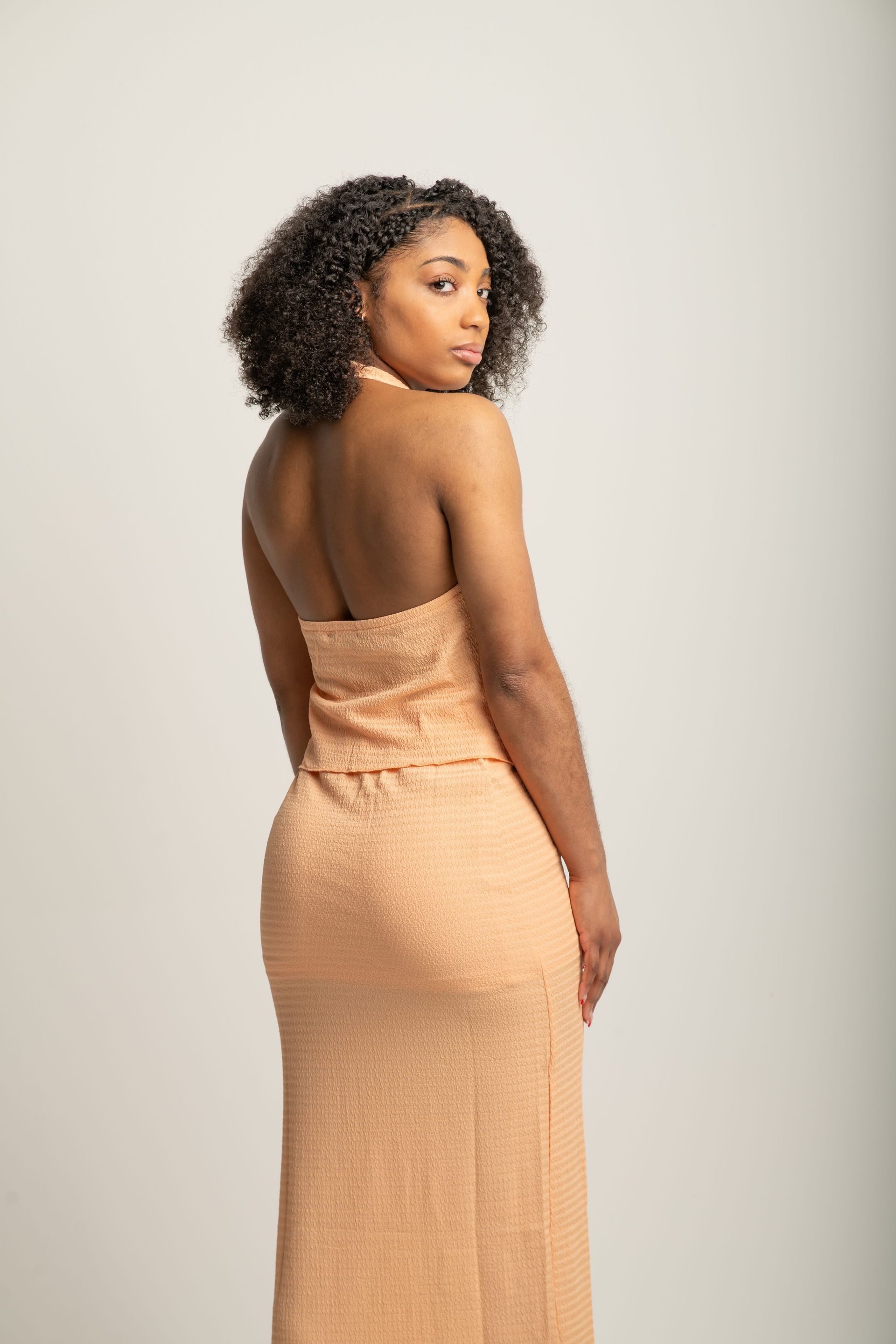 Woman in a peach dress standing in profile against a plain light background