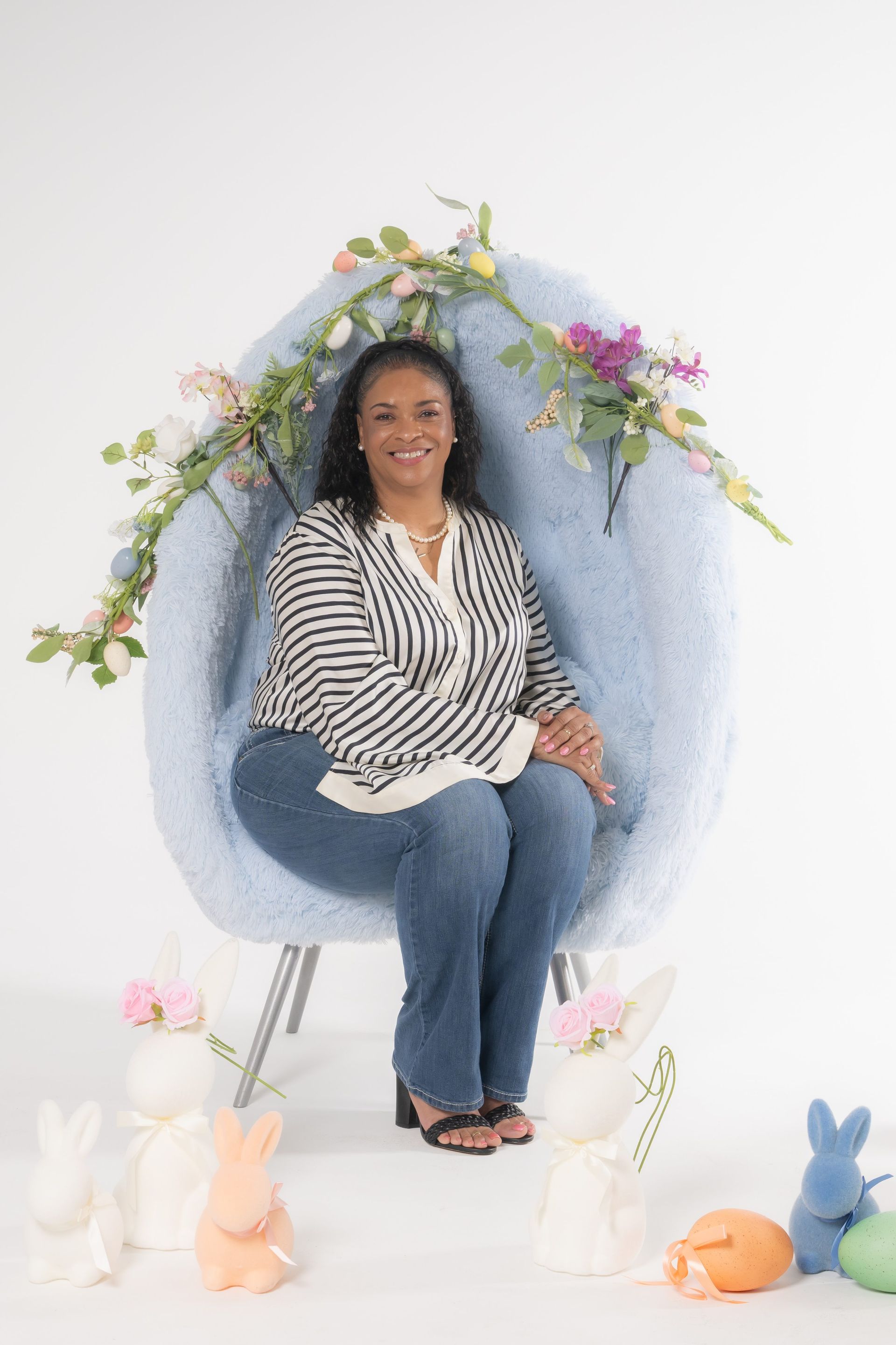 Woman seated in a blue chair surrounded by pastel flowers and bunny decorations