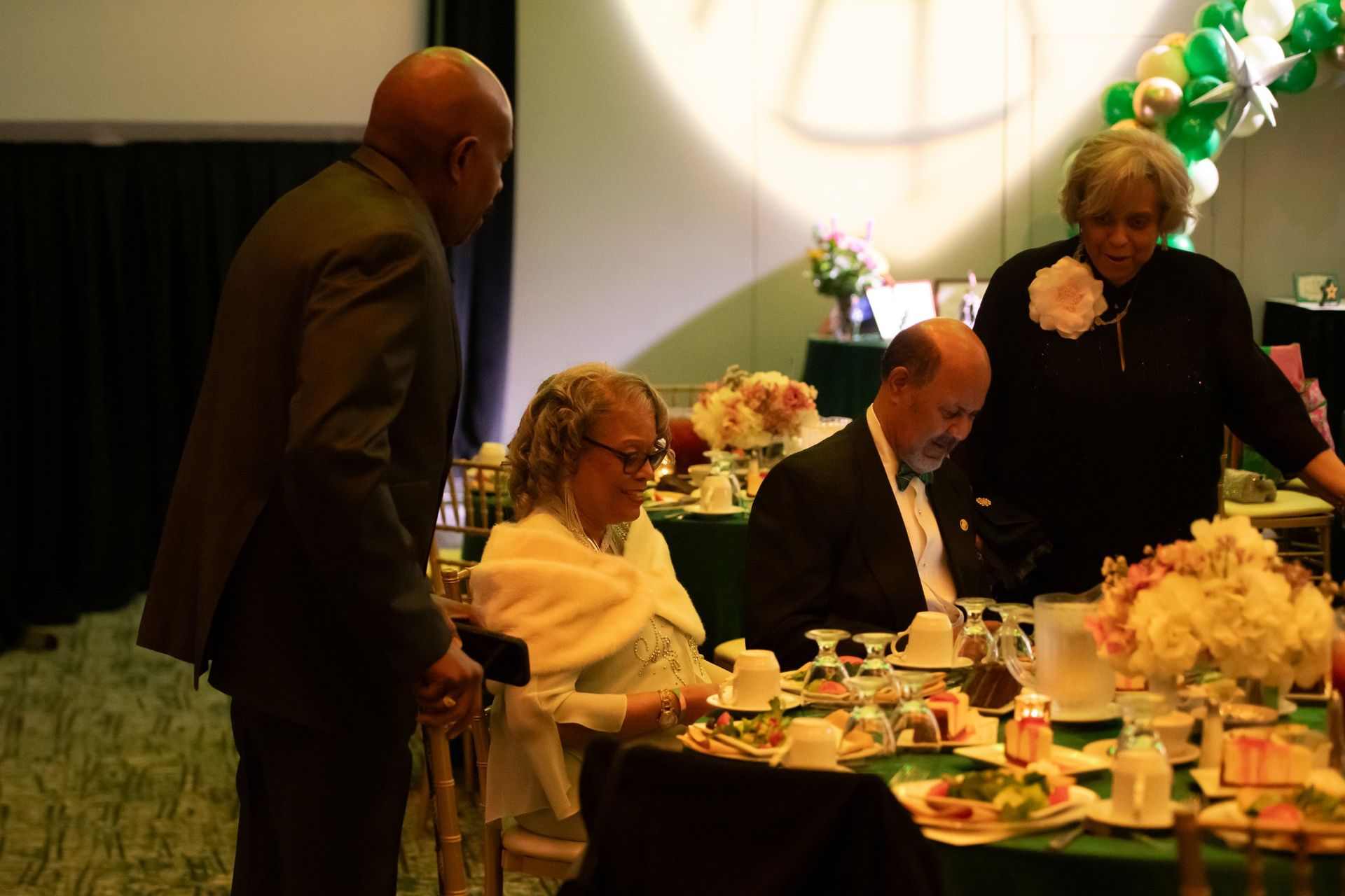 People seated at a banquet table with floral centerpieces, while servers stand nearby in a warmly lit event hall
