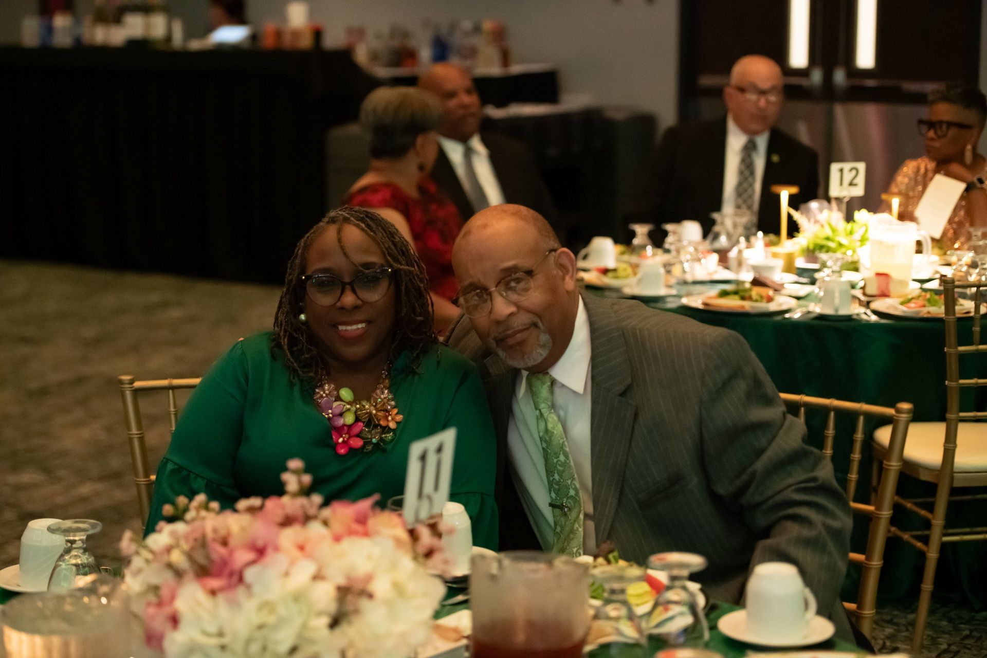 Two people smiling at a banquet table with flowers and table number 11 at a formal event