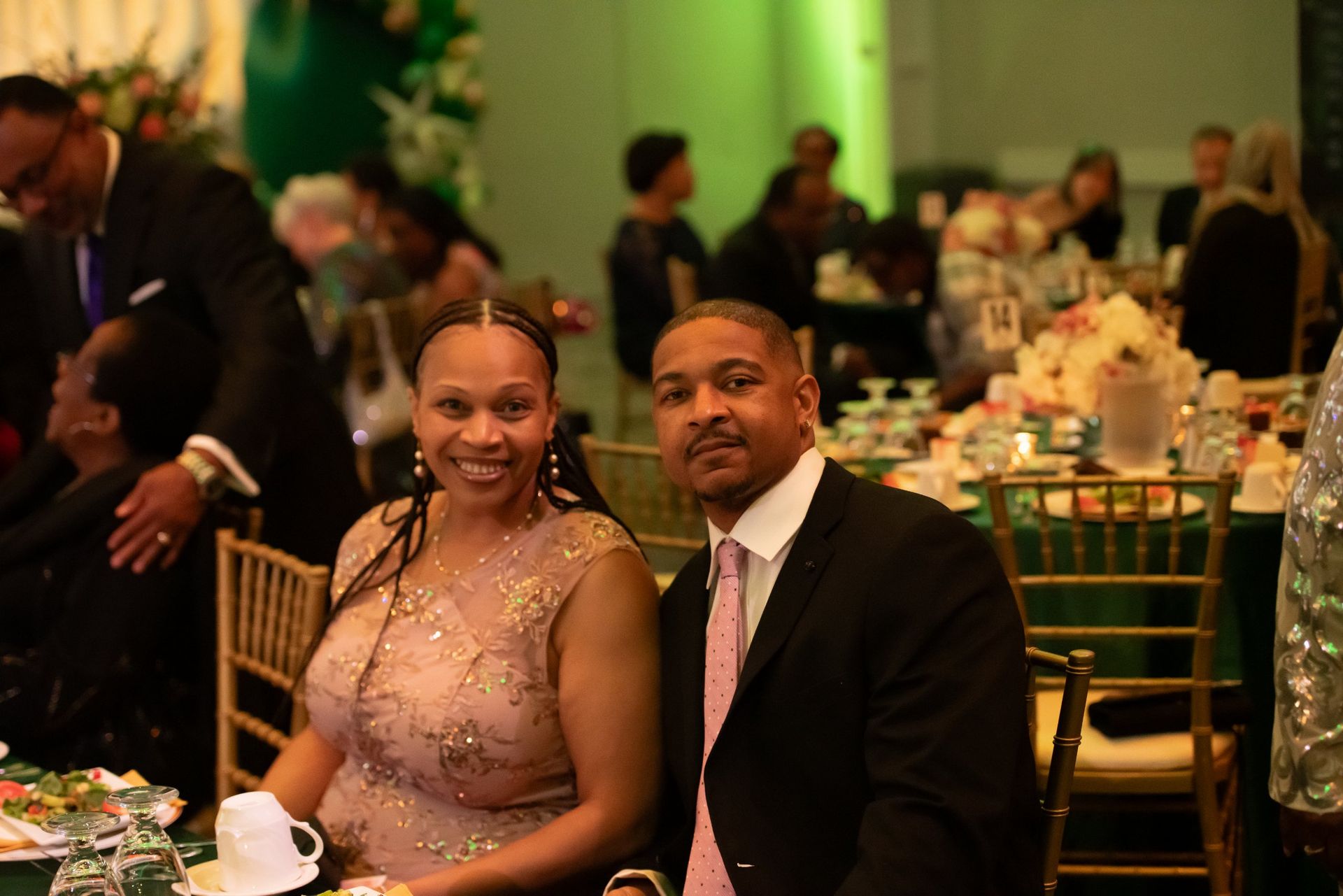 Couple seated at a formal banquet table, smiling in a warmly lit reception hall.