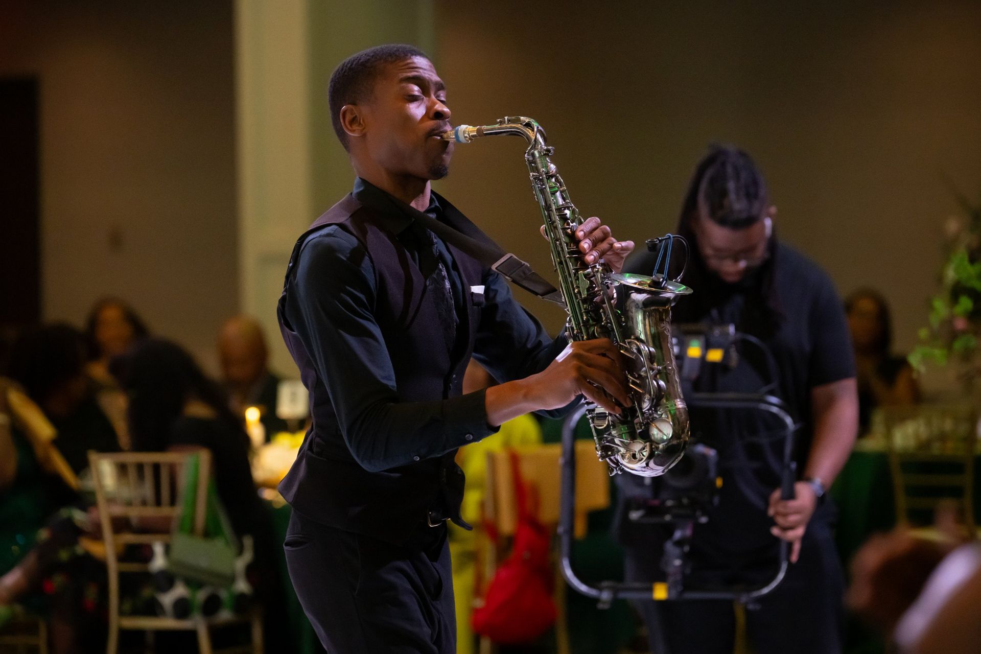Saxophonist playing on stage while another musician adjusts equipment in the background