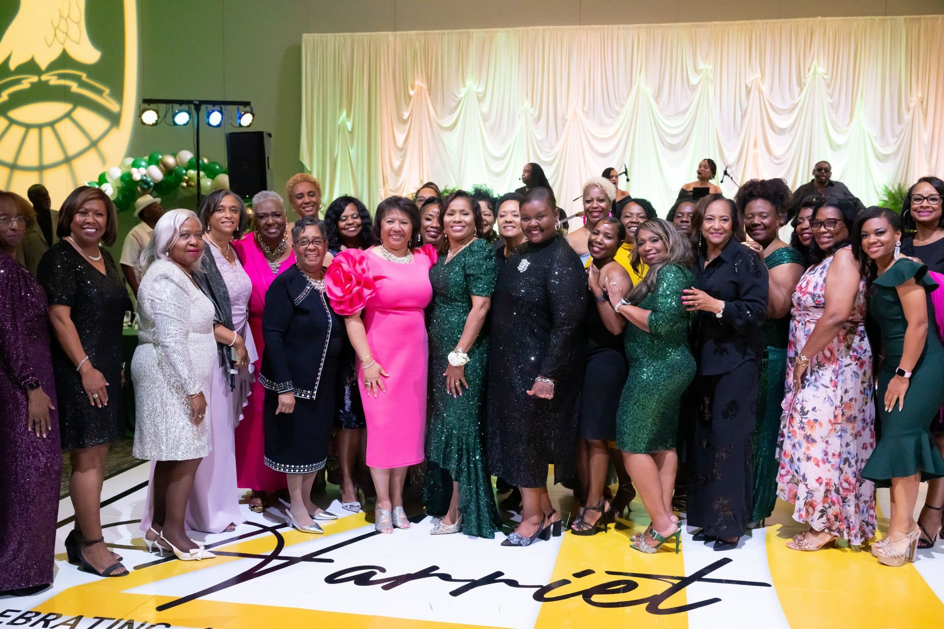 Group of women in formal dresses posing at a celebration in a decorated banquet hall.