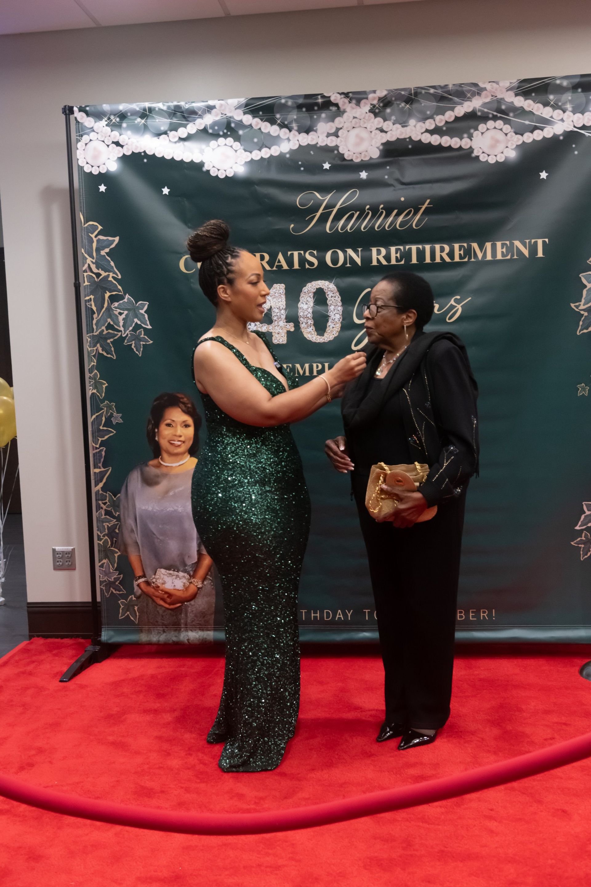 Two women pose on a red carpet in front of a retirement event backdrop.