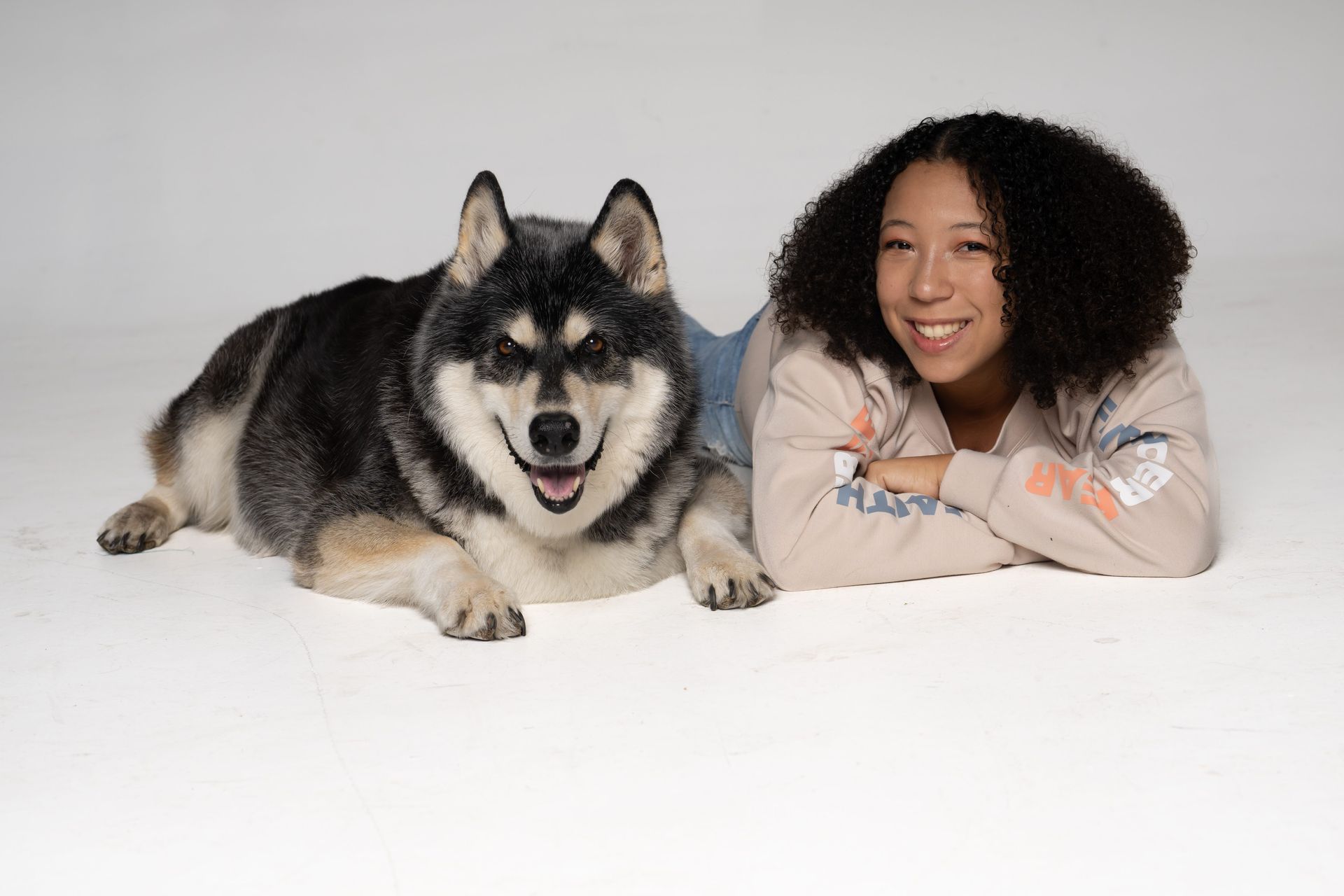 Woman lying next to a fluffy black-and-tan dog on a white floor, both facing the camera.