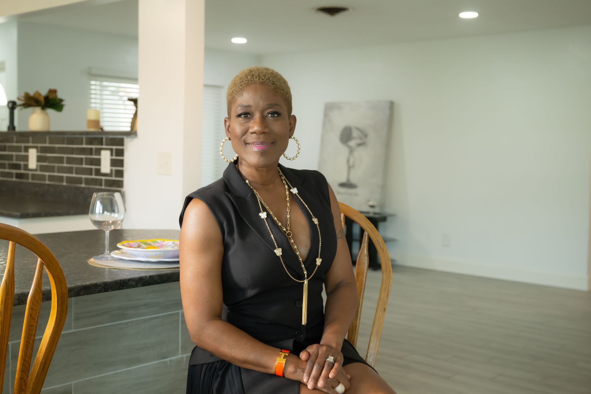 Woman seated at a kitchen island in a bright modern home, wearing a black dress and smiling