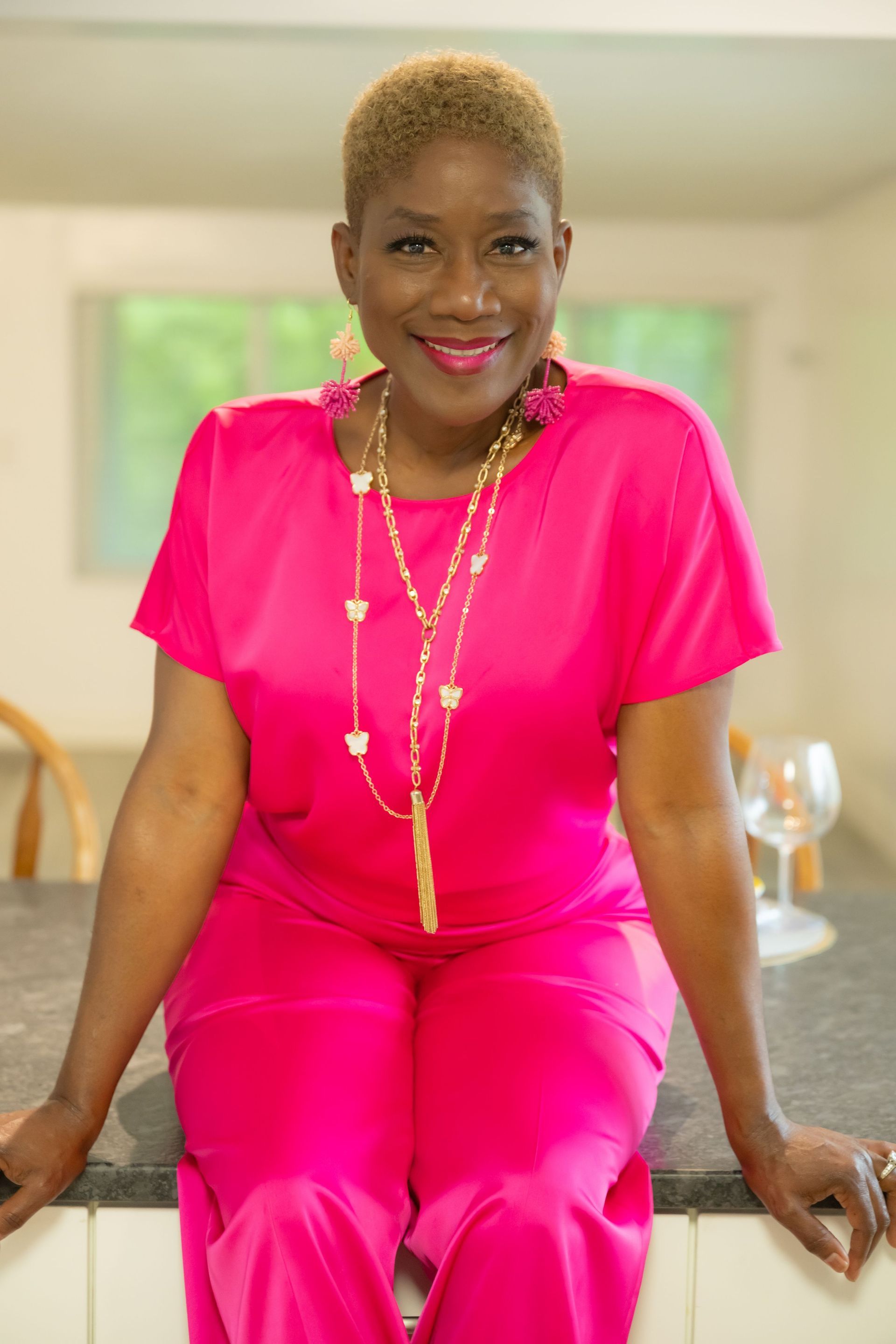 Woman in bright pink outfit sitting indoors, smiling at the camera.