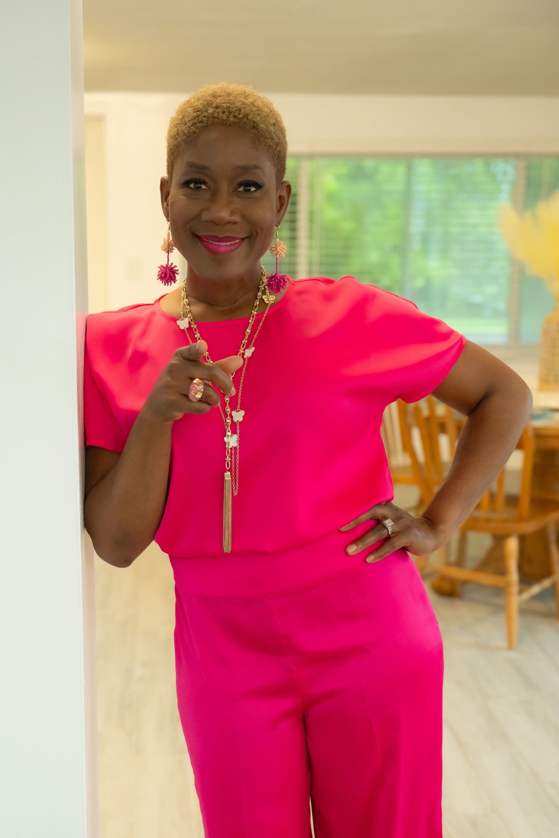 Woman in bright pink outfit posing indoors with hand on hip and holding a lanyard.