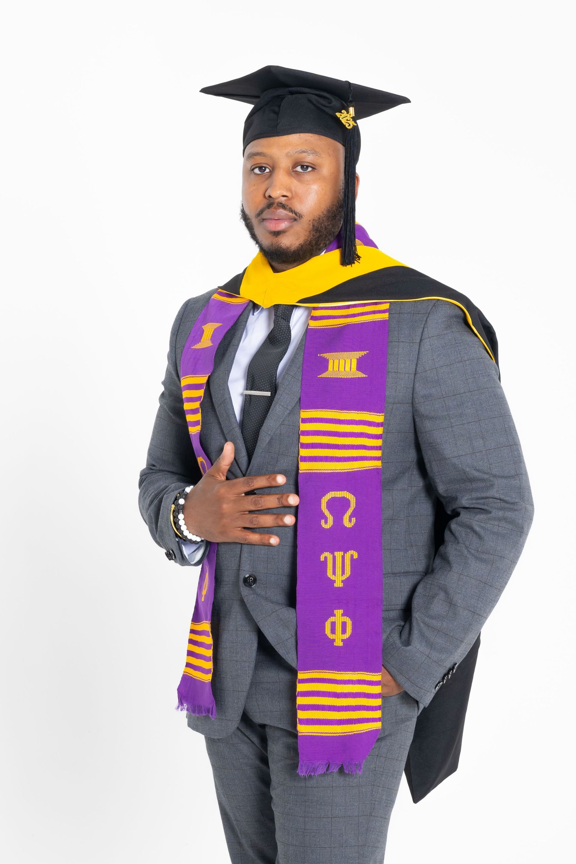 Graduate in cap and gown with purple-and-gold stole, holding a diploma against a white background