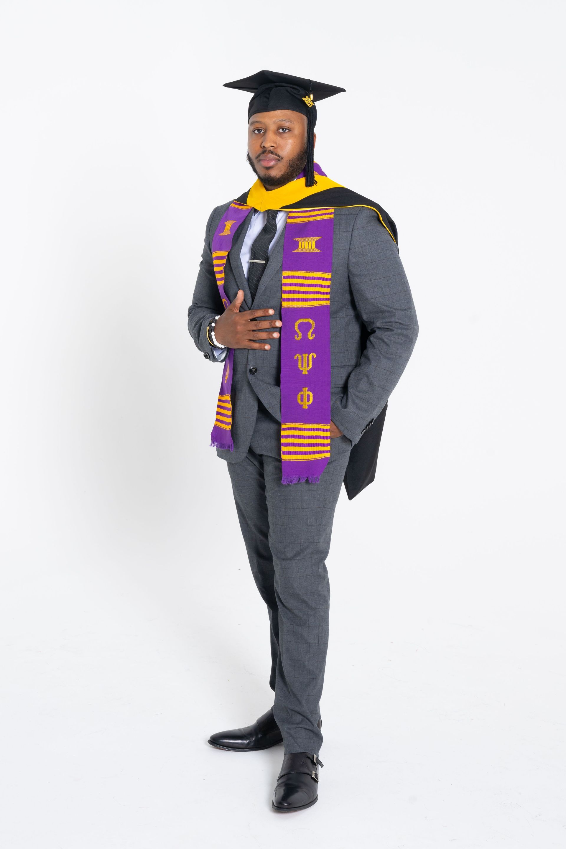 Graduate in cap and gown standing against a white background, holding a diploma.
