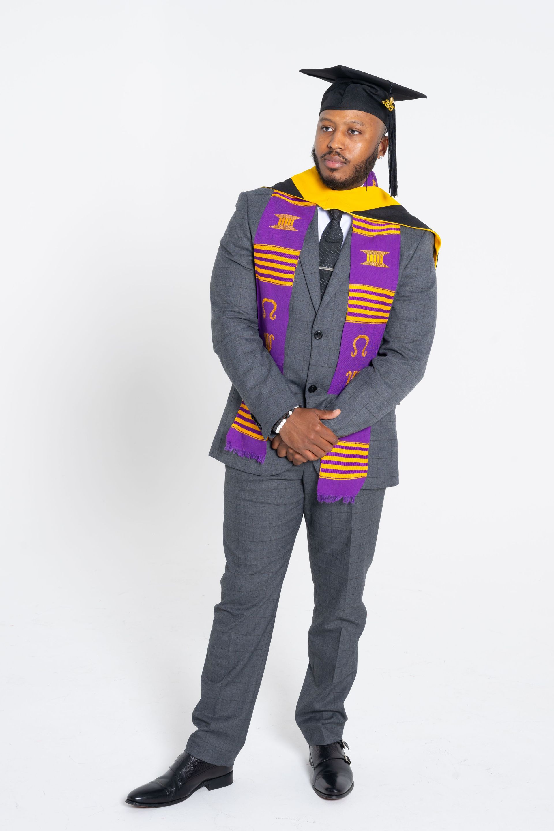 Graduate in gray suit, black cap, and purple stole standing against a white background.