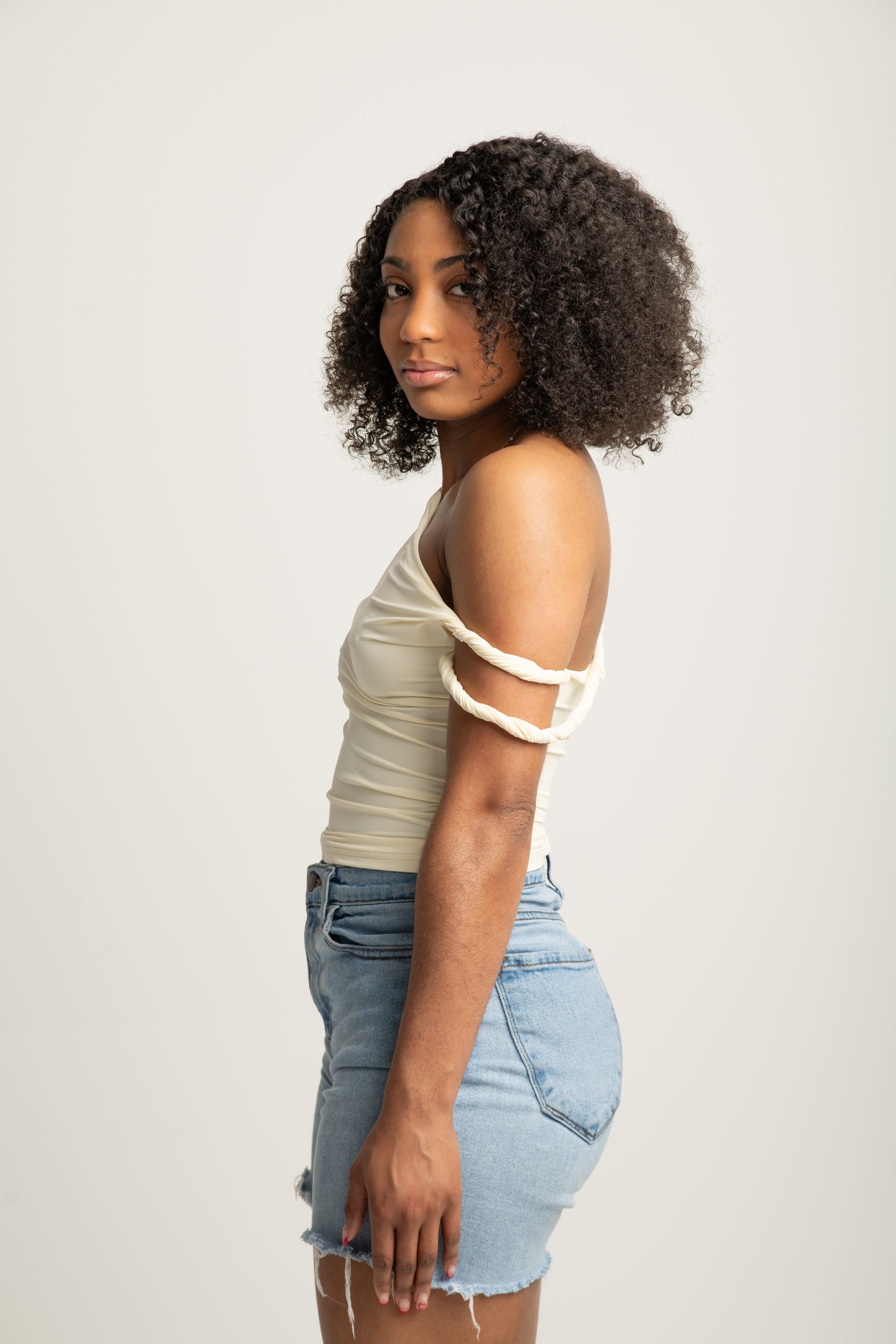 Side view of a person in a beige top and denim shorts, standing against a plain light background.