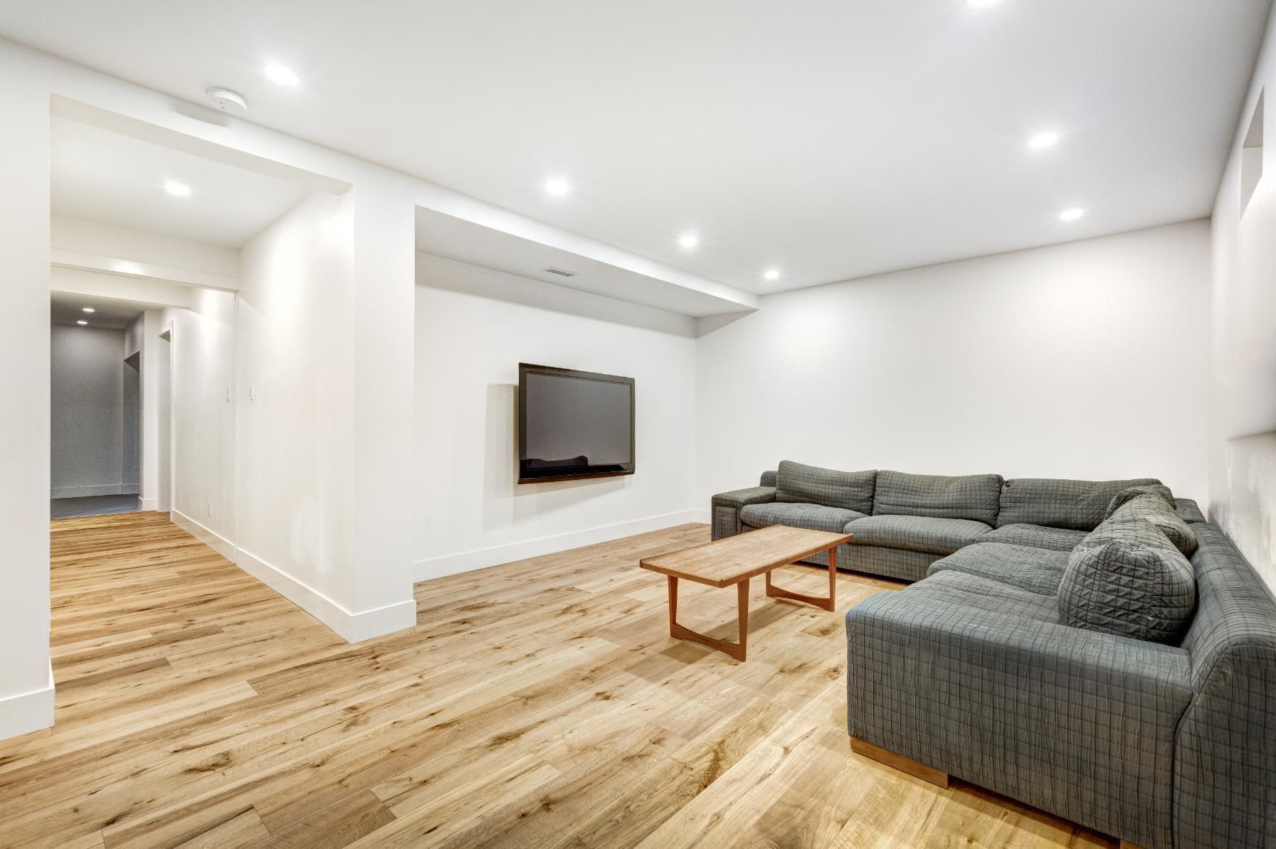 Modern living room with light wood floors, gray sectional sofa, and wall-mounted TV.