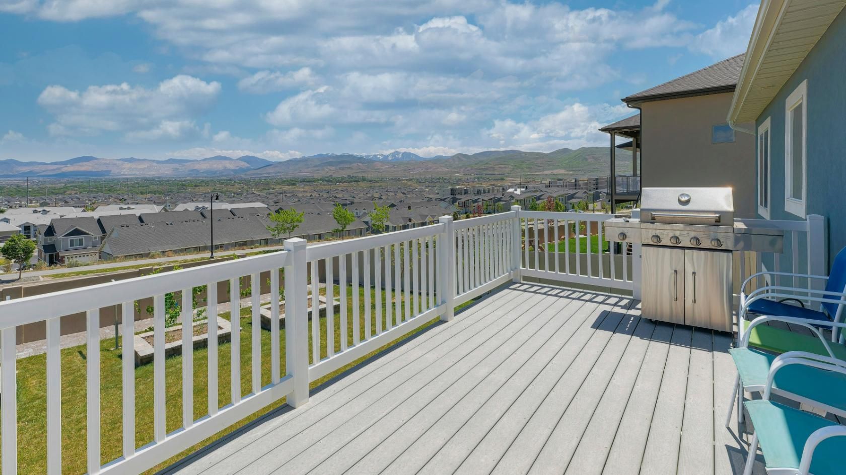 Wooden deck with white railing and built-in grill, overlooking a green yard and distant hills under a cloudy sky.
