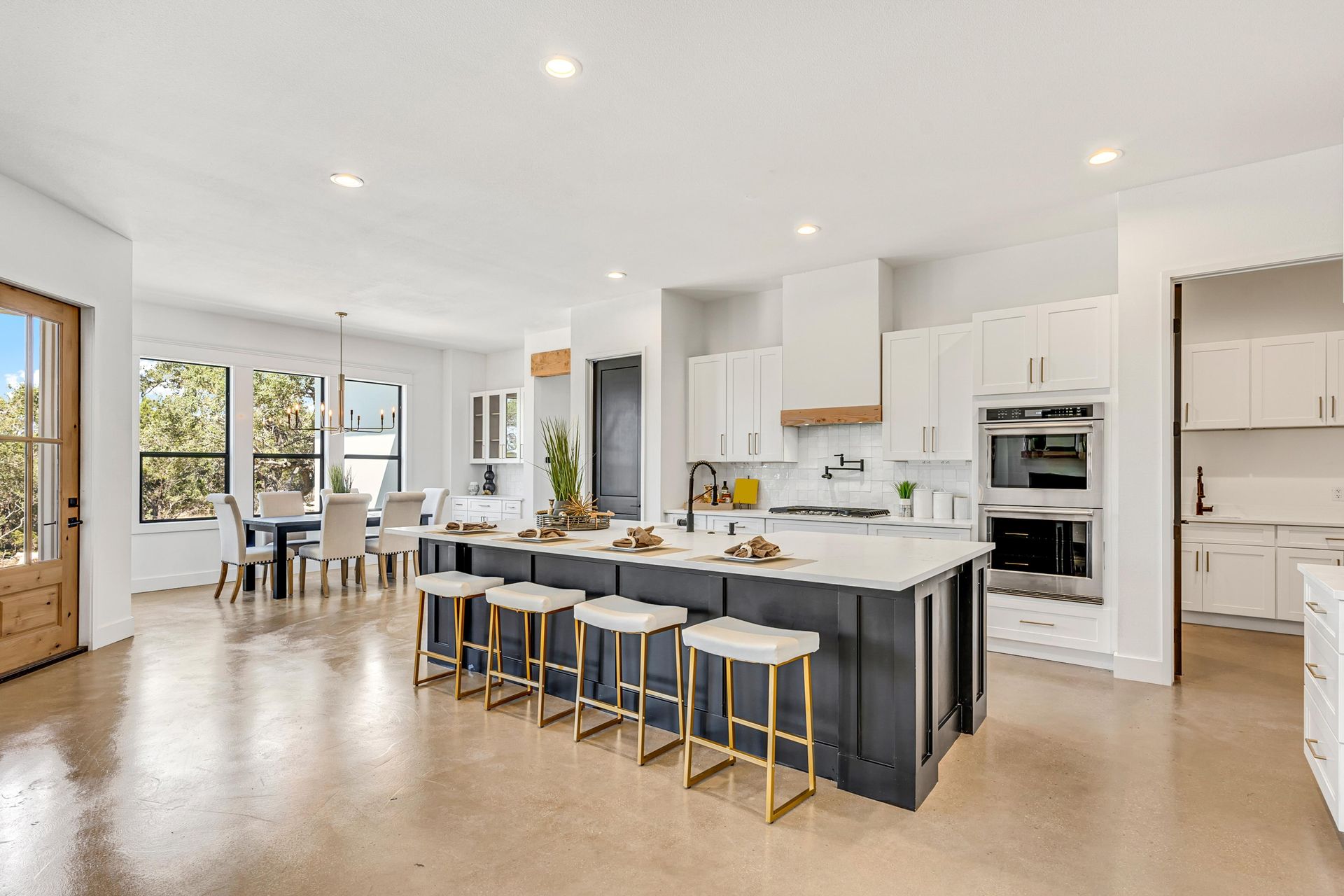 Open-concept kitchen with large island, seating, and white cabinets. Dining area and outdoor light visible.